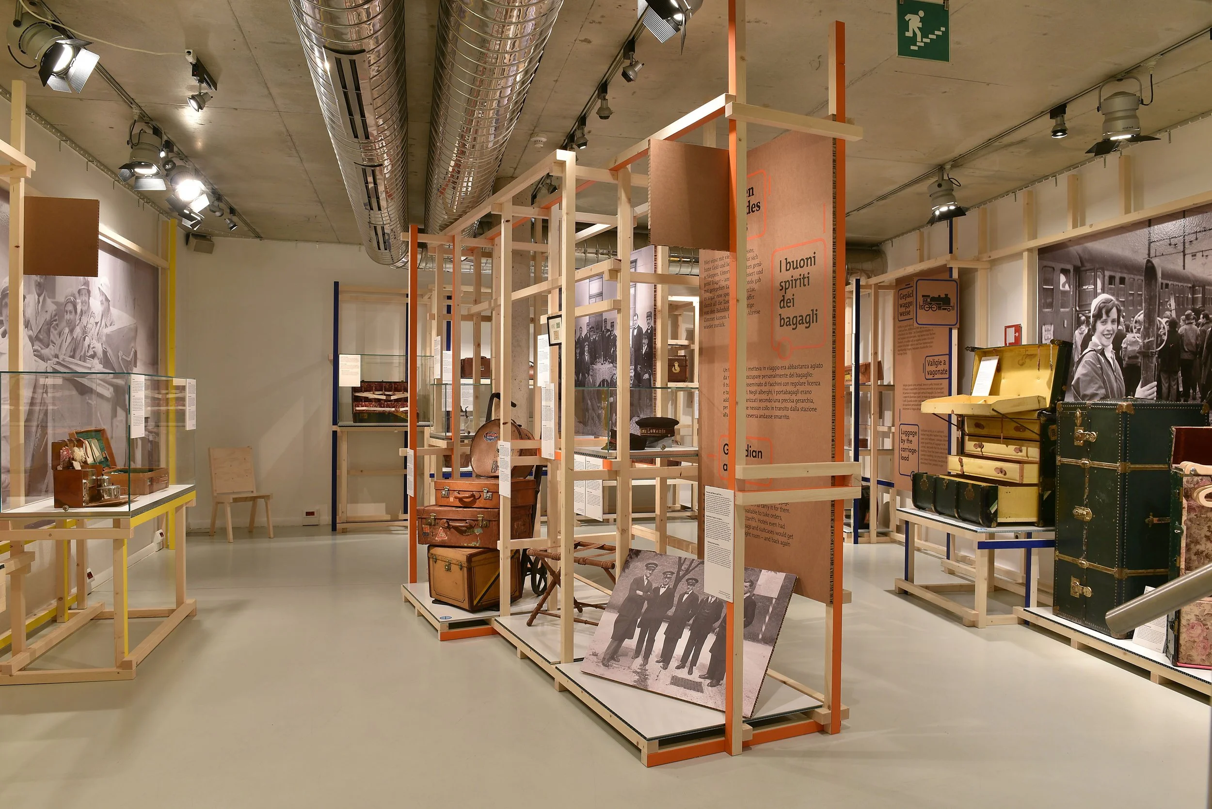 Ausstellung mit gebrauchten Gepäckstücken und historischen Fotografien in einem Museum, Holzkonstruktionen und Informativtafeln