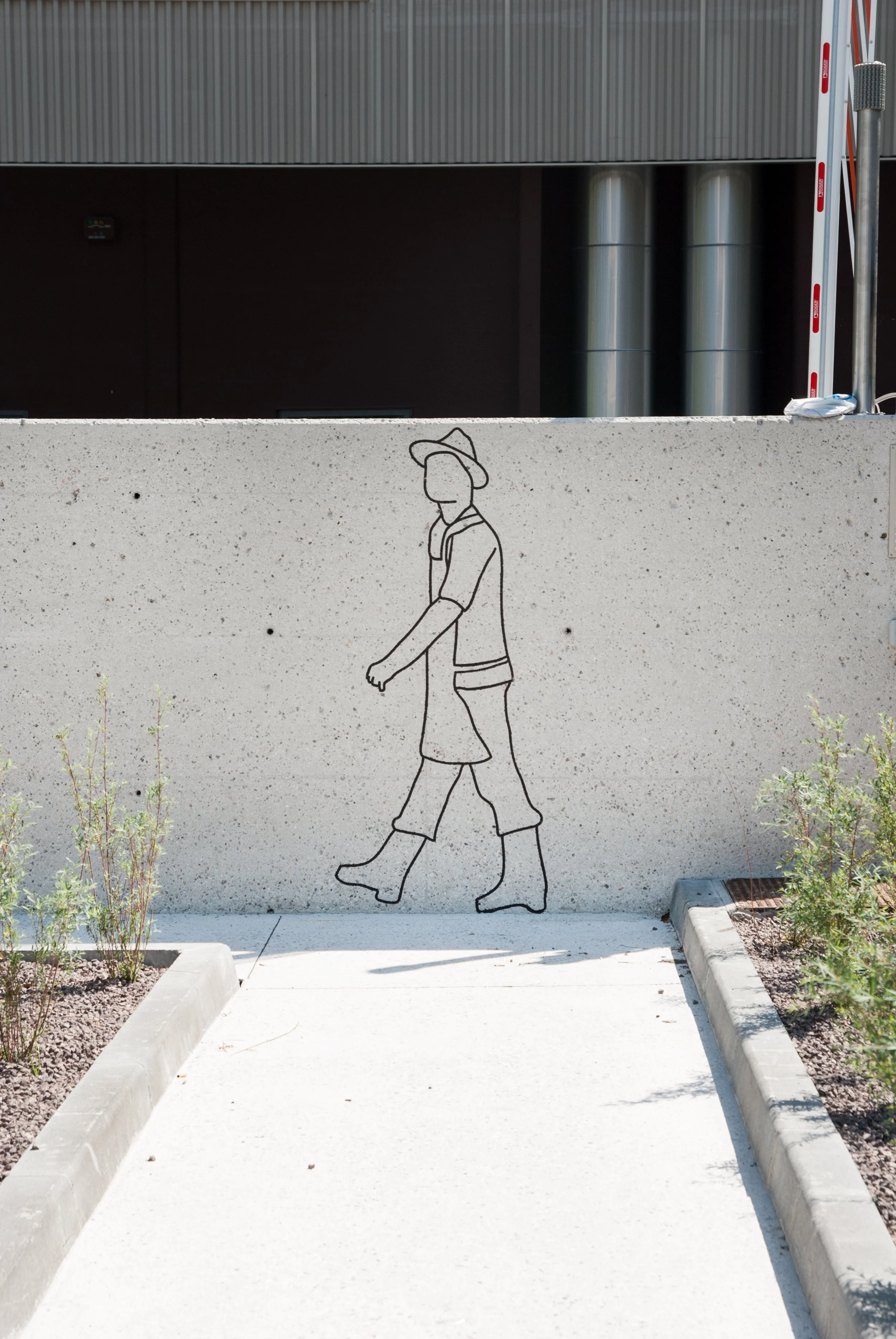 Strichzeichnung eines Mannes mit Hut, ausgestrecktem Arm und Beinen, auf einer Betonmauer im Freien, flankiert von Pflanzen.