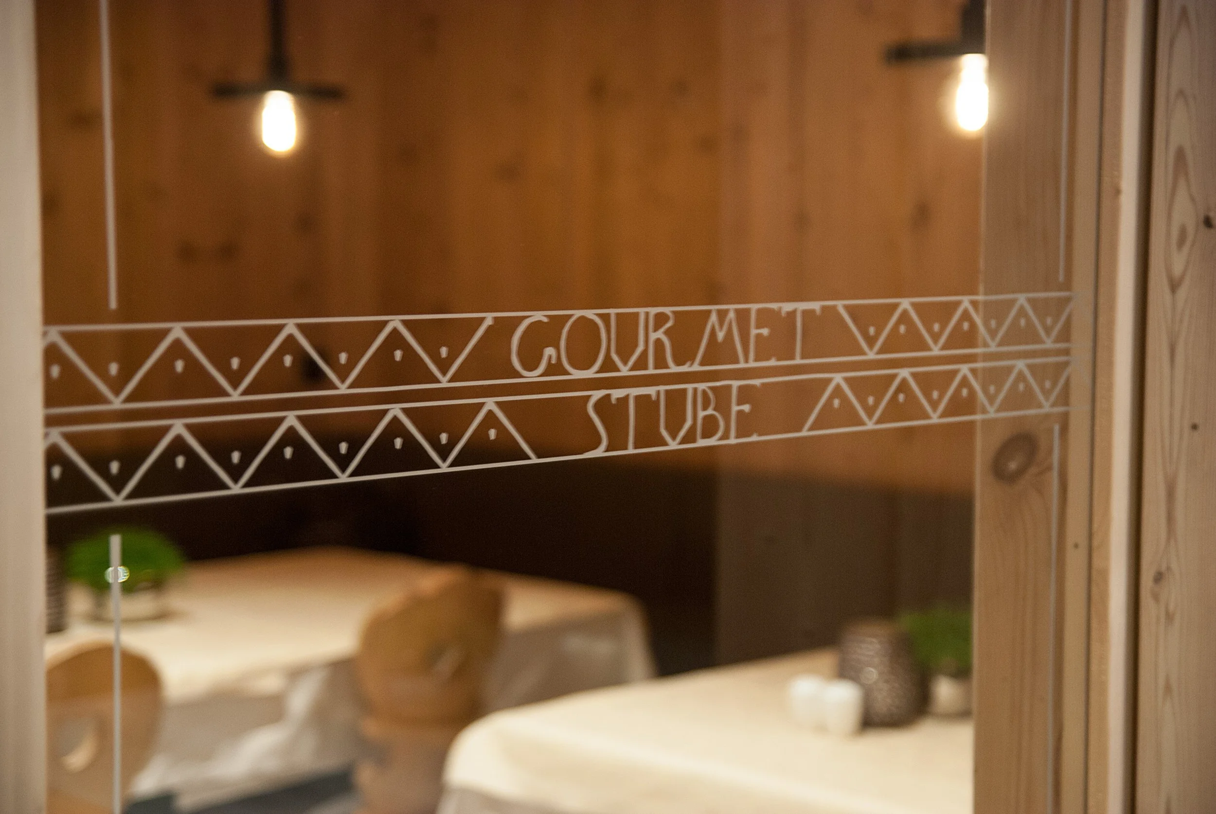 Innenansicht eines Restaurants mit Holzwänden, Tischen und Stühlen, reflektiert im Spiegel mit der Aufschrift 'Gourmet Suite' in weißen Linien.