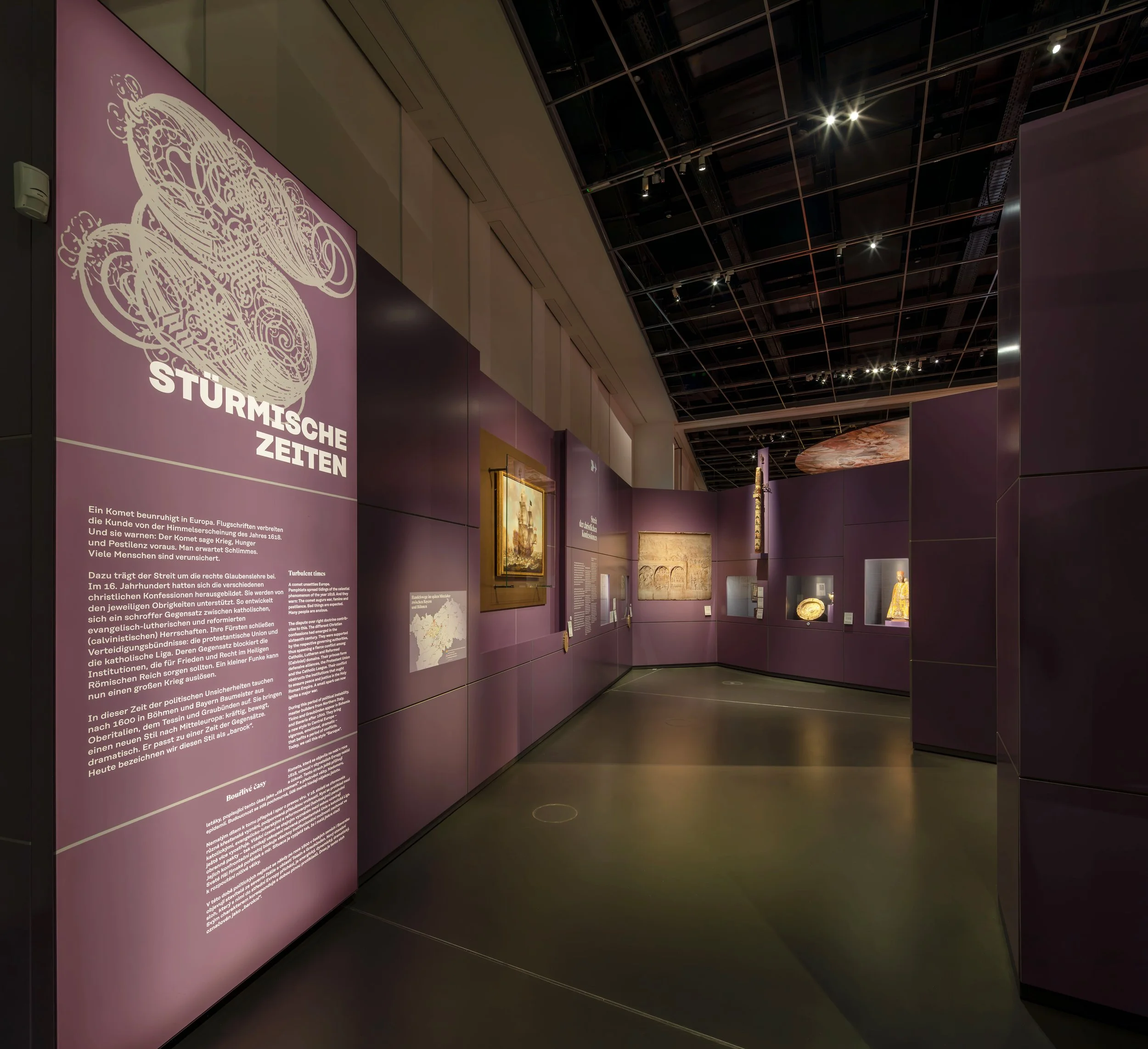 Ausstellung im Museum mit einer großen Informationstafel auf der linken Seite, die den Titel 'Sturmische Zeiten' trägt, und mehreren Kunstwerken an der Wand, die in einer dunklen, modern gestalteten Galerie präsentiert werden.