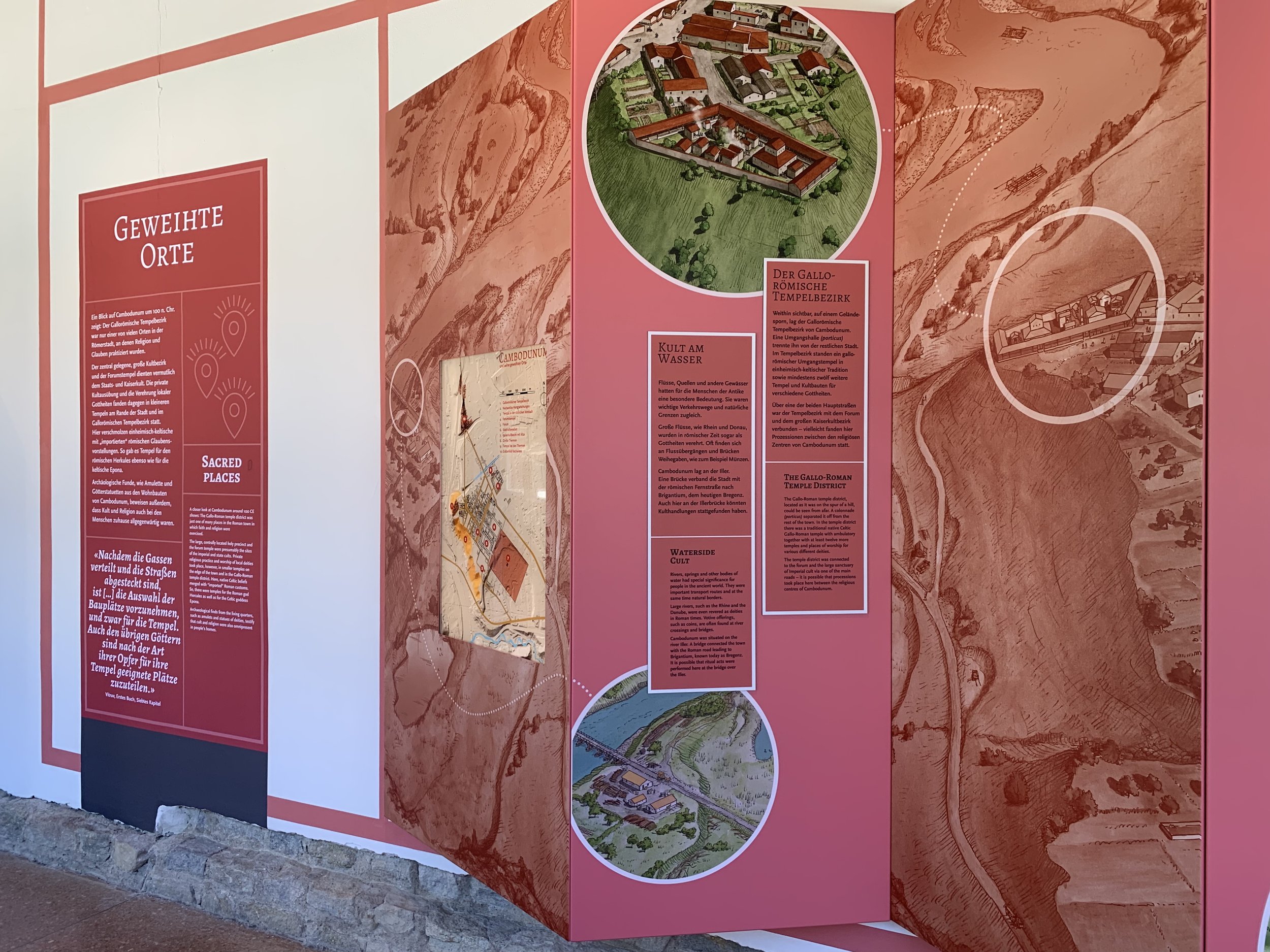 Informationsschild mit Themen zu heiligen Orten, Wasser- und Tempelbezirk, inklusive Karten und Illustrationen, an einer pinken und roten Wand.