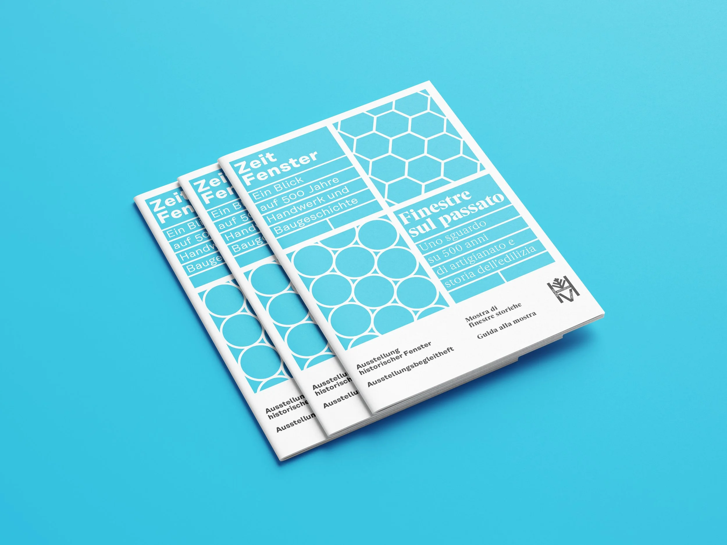 Drei Broschüren liegen übereinander auf einem blauen Hintergrund. Die Broschüren haben einen hellblauen und weißen Cover mit geometrischen Mustern und Text in mehreren Sprachen.