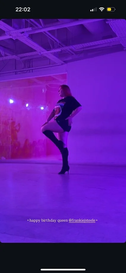 Person dancing in Nottingham or posing in a room with purple lighting, wearing high-heeled boots and black shorts, with text that says "happy birthday queen @frankiejsteele".