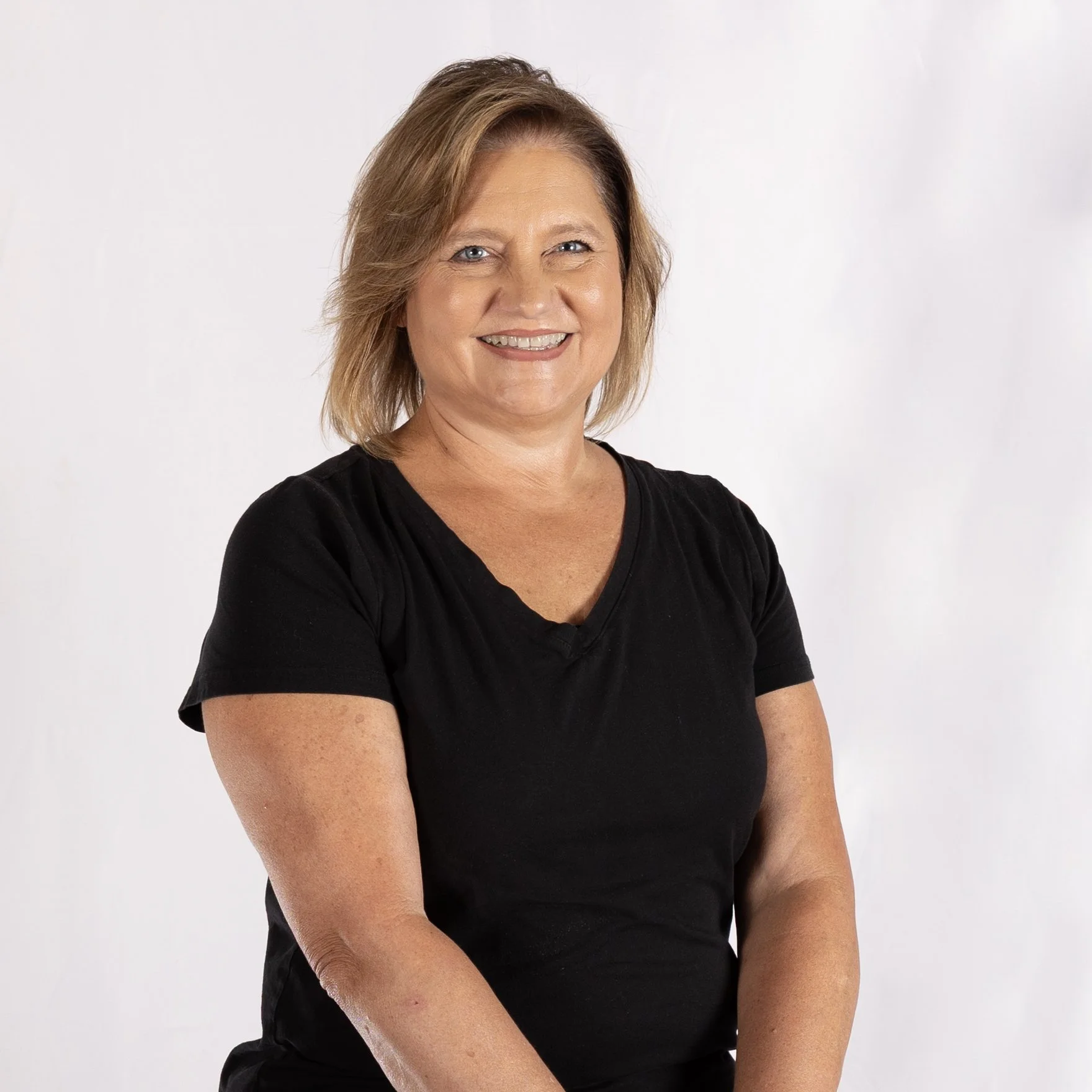 A woman with shoulder-length light brown hair wearing a black t-shirt and smiling, posing against a plain white background.