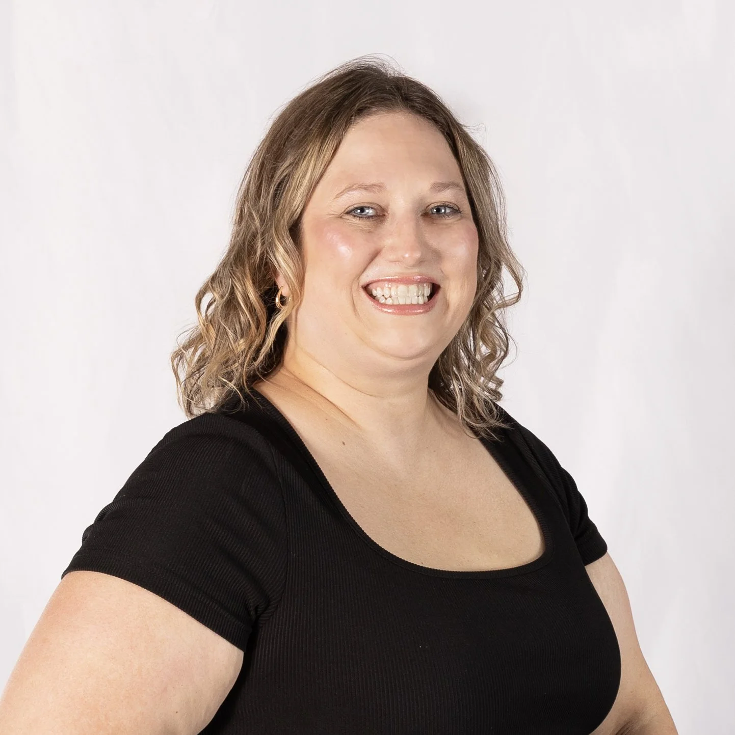 A woman with wavy, shoulder-length hair smiling and wearing a black top against a plain white background.