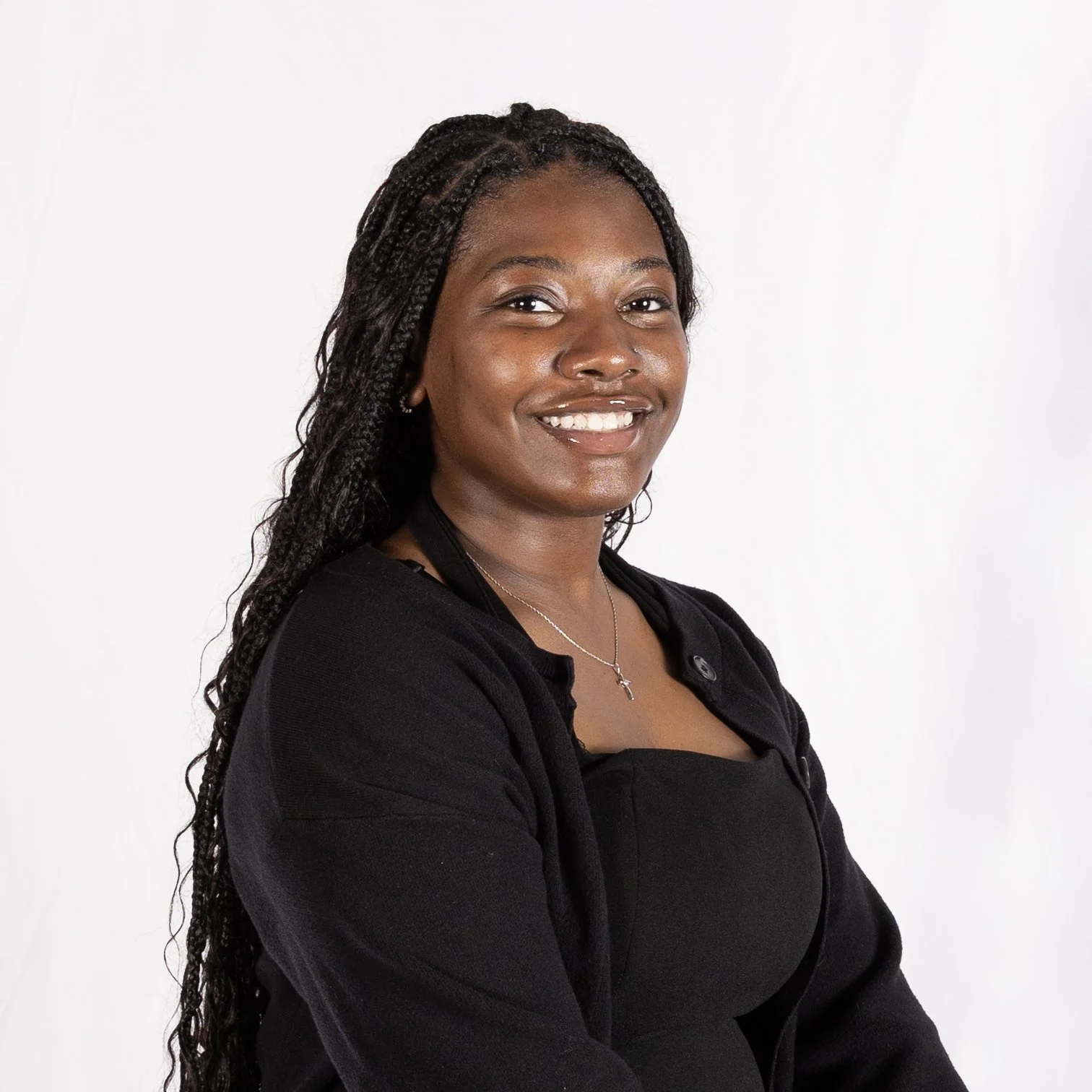 A woman with long braided hair smiling in front of a white background.