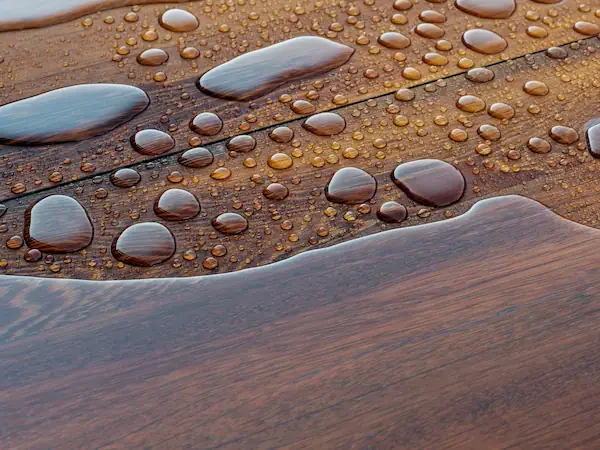 Gros plan sur l'effet perlant de l'eau sur une terrasse en bois traitée avec un saturateur professionnel.
