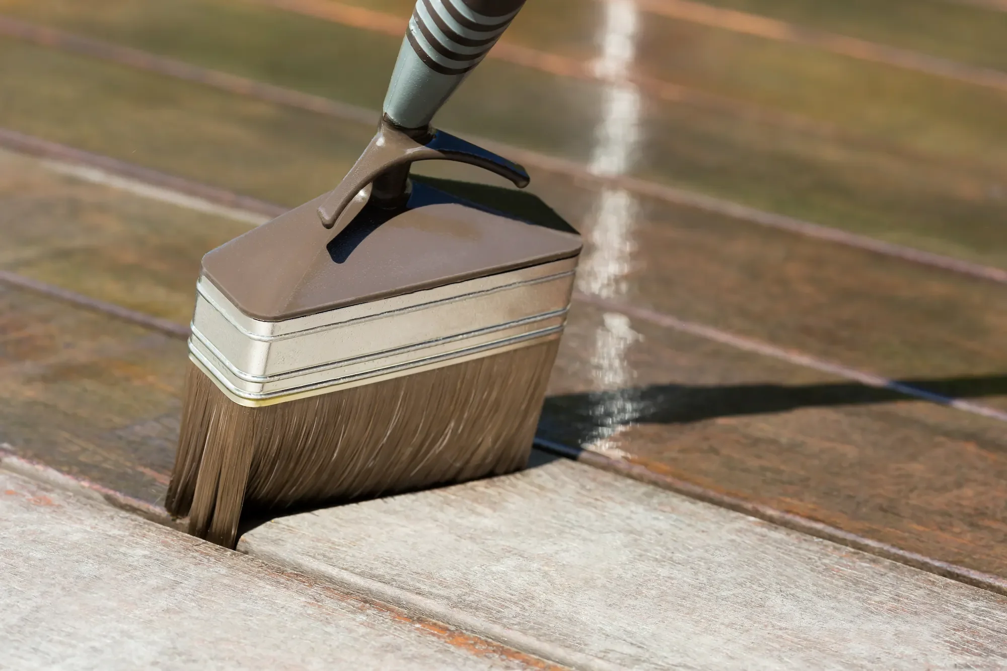 Application précise à la brosse d’un produit dégriseur sur les lames de bois d’une terrasse à Arles.