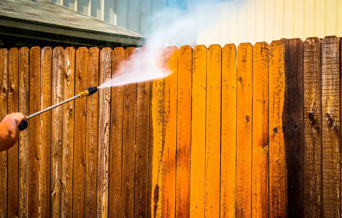 Clôture en bois nettoyée avec un jet à pression maîtrisée pour retrouver sa couleur d'origine.