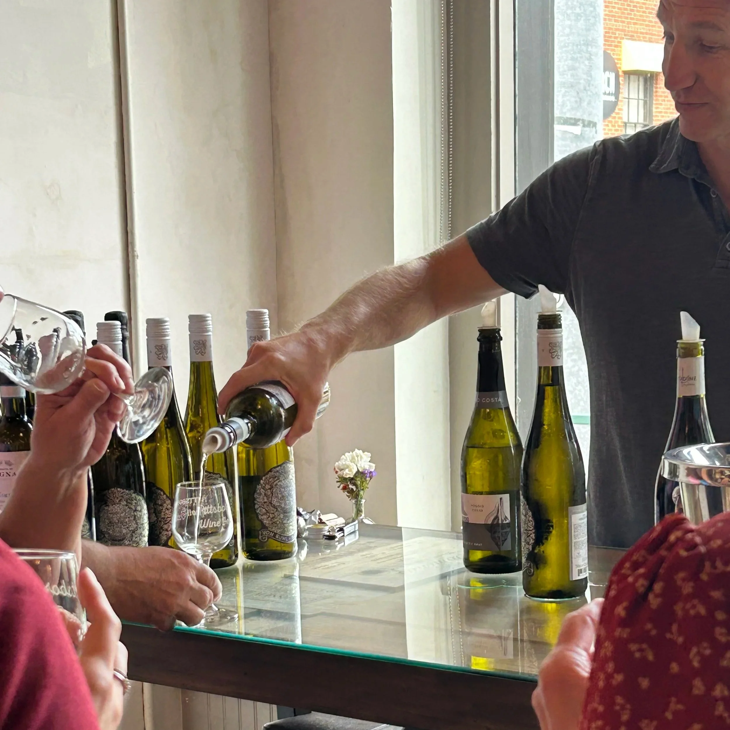 Man pouring white wine into glasses at a wine tasting event.