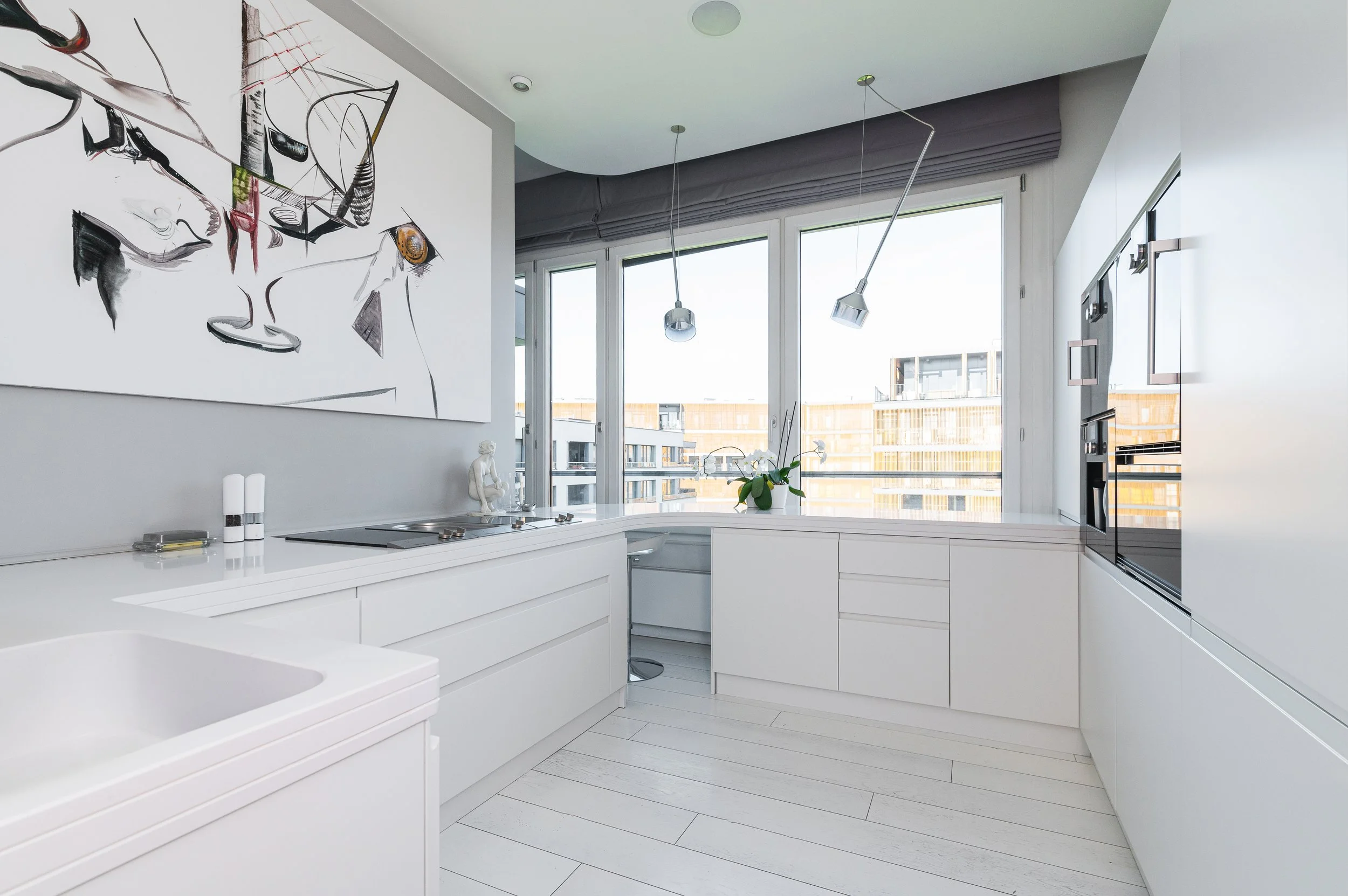 Modern white kitchen with a large window, abstract wall art, and pendant lighting fixtures.