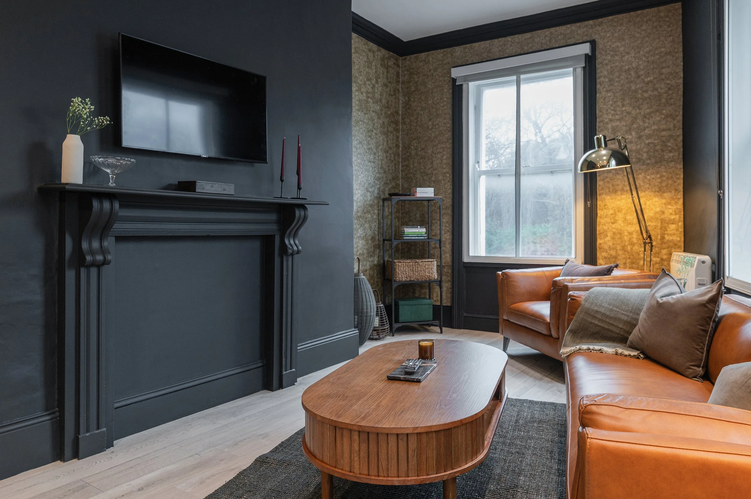 Living room with dark gray and beige walls, large window, leather couch, wooden coffee table, and television.