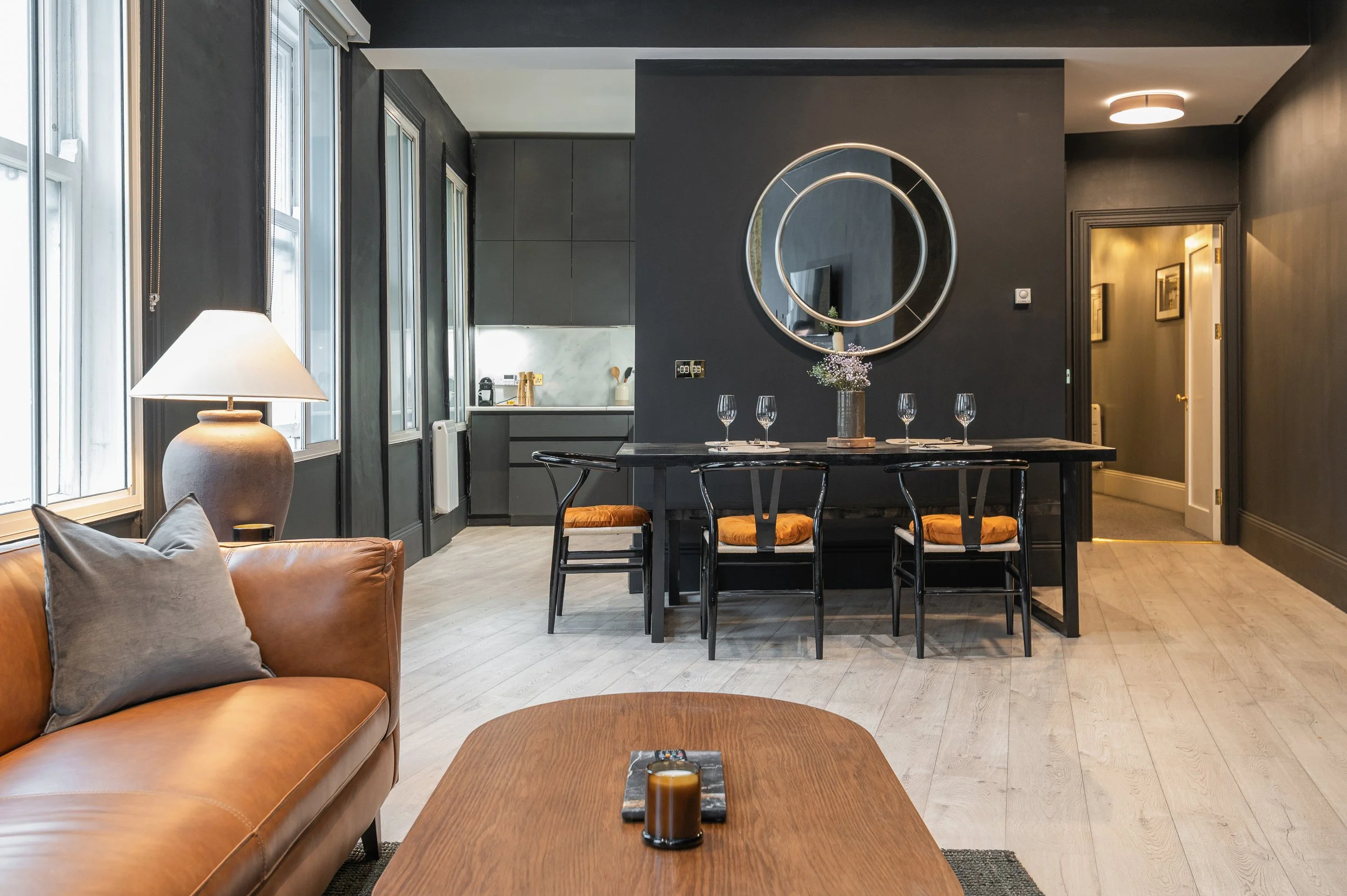 Interior of a modern living and dining area with a leather sofa, wooden coffee table, dining table with four chairs, large mirror, and various decor items in a contemporary home.