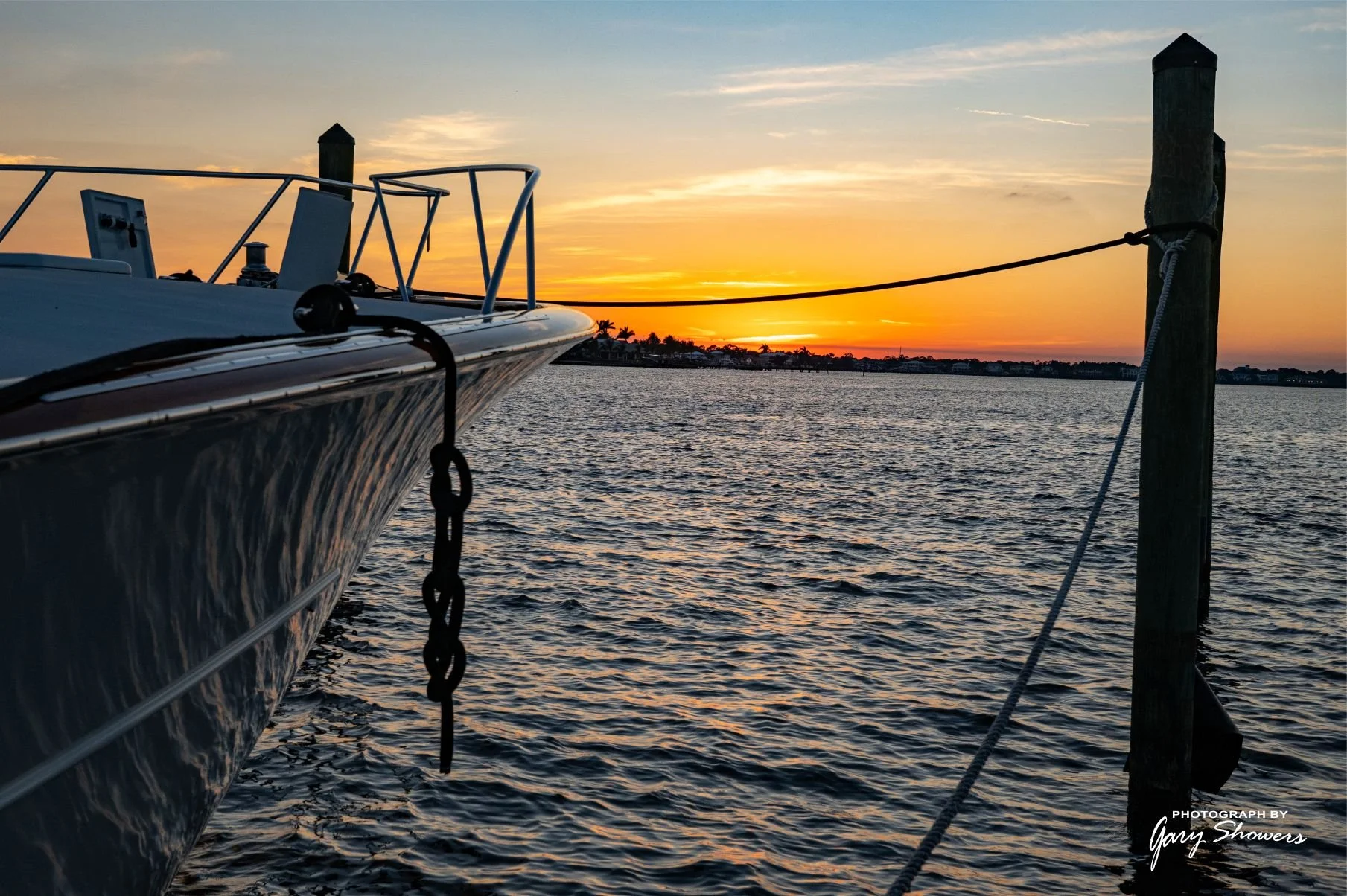 Sailboat moored at a dock during sunset, with calm water and a colorful sky.