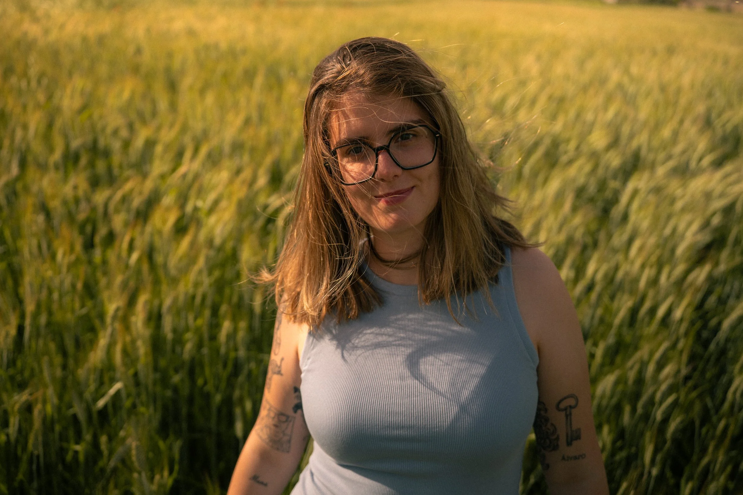 Juventud con lentes en campo de trigo al atardecer.