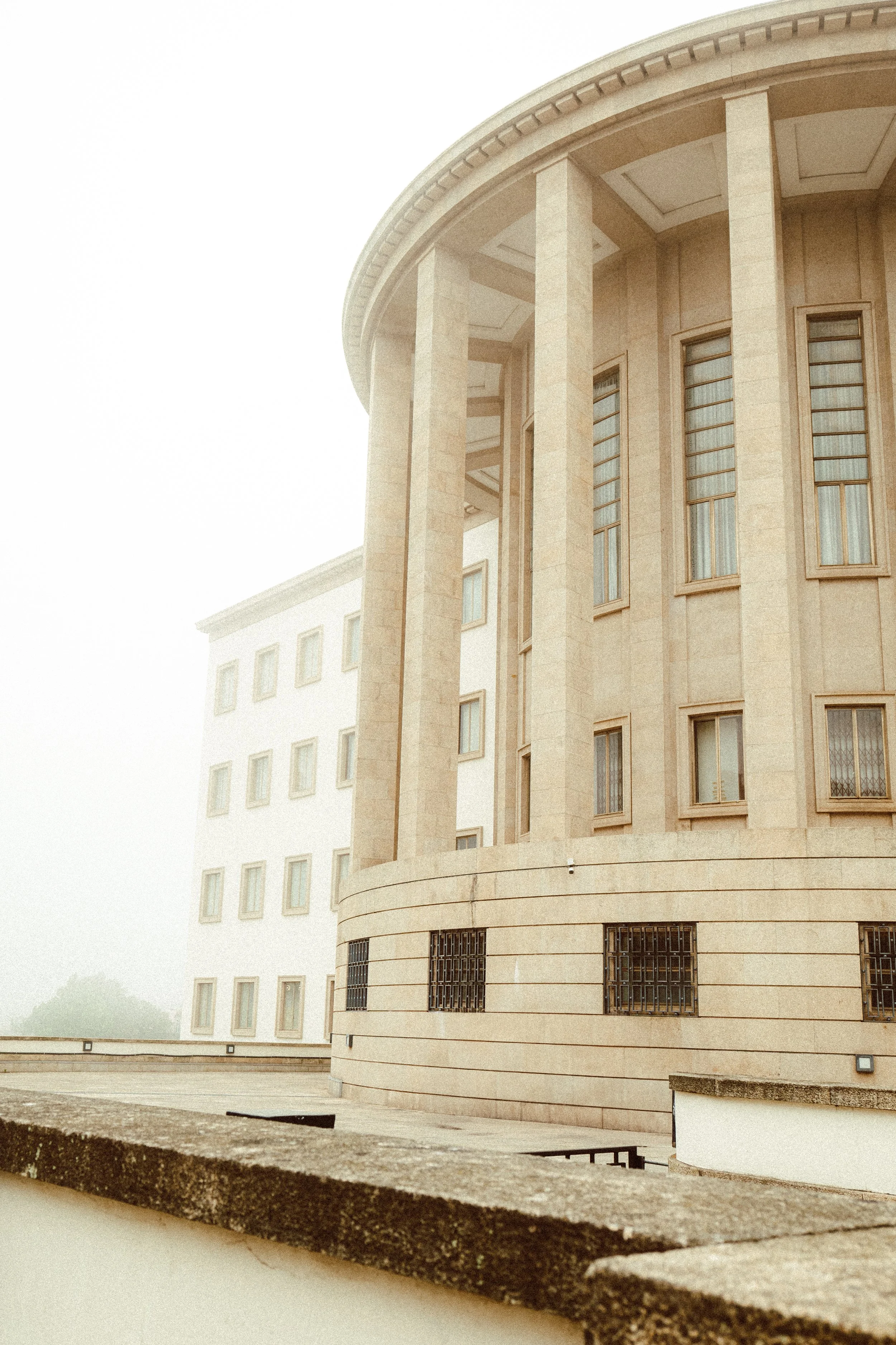 Edificio de arquitectura clásica con columnas y ventanas en la fachada, envuelto en una niebla suave.
