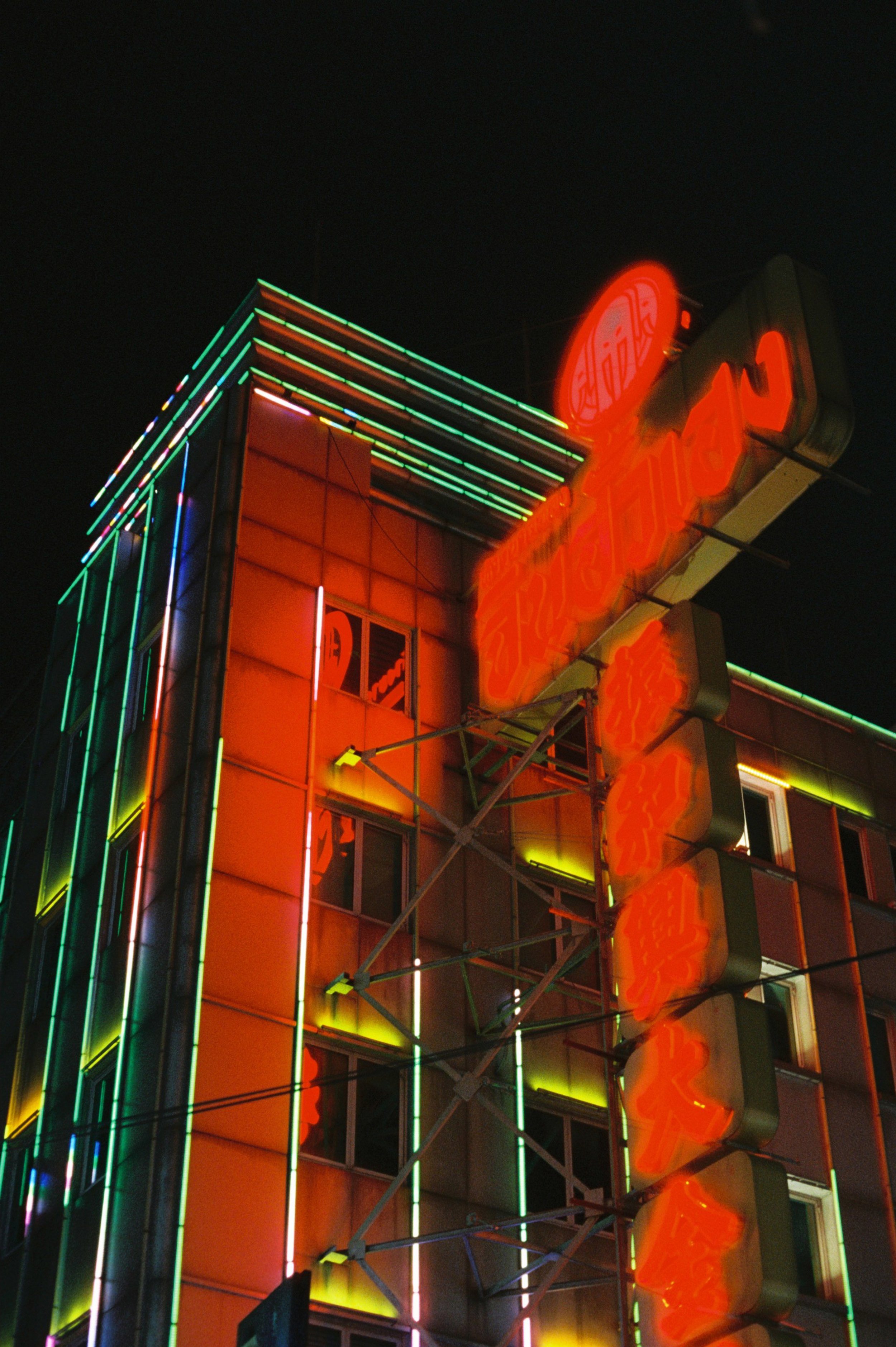 Edificio iluminado con neón de colores en la noche, con cartel grande en estilo retro.