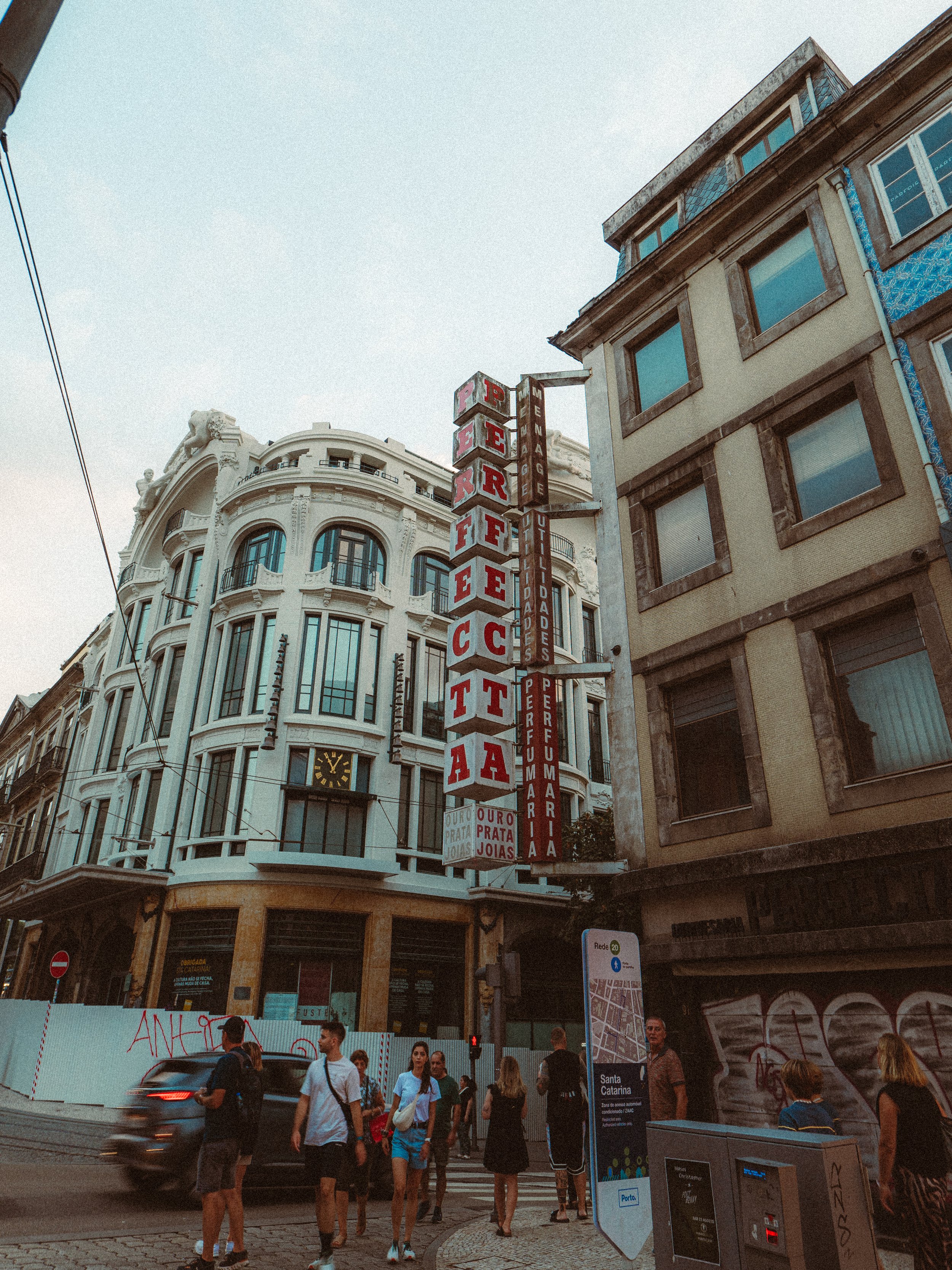Edificio histórico en el centro de la ciudad con cartel de tienda que dice Perfumería y joyas, con personas cruzando la calle en un día nublado en Santa Catarina.