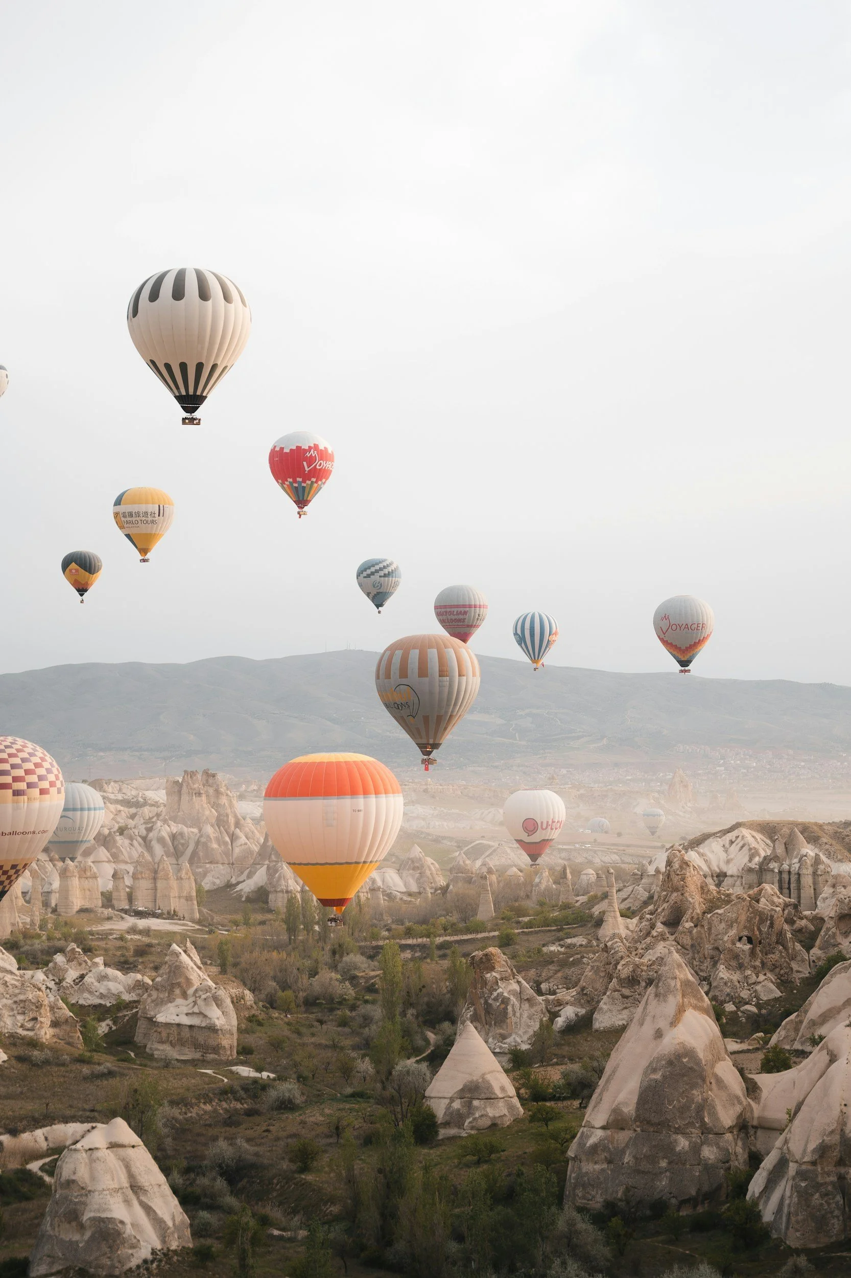 Multiple hot air balloons floating over a rocky landscape with distinctive rock formations and sparse vegetation.