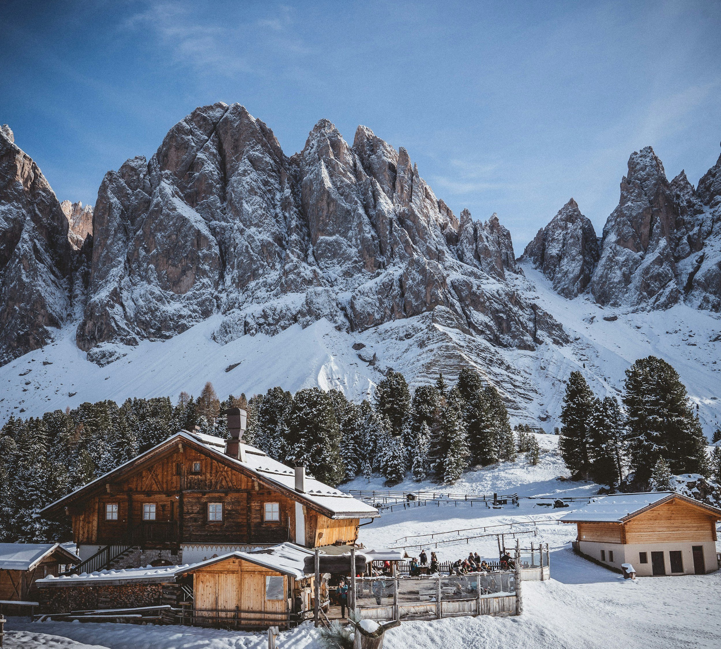 Snow-covered mountains backdrop with a wooden cabin and other small buildings in a winter landscape.