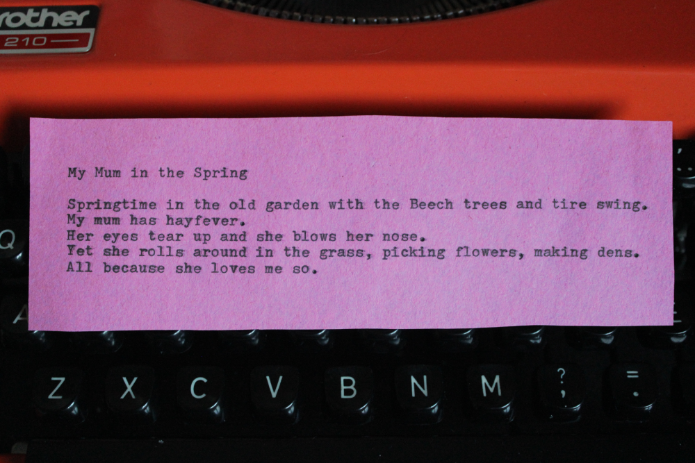 Pink note paper with a poem about a mother in spring, placed on the black keys of an orange typewriter.