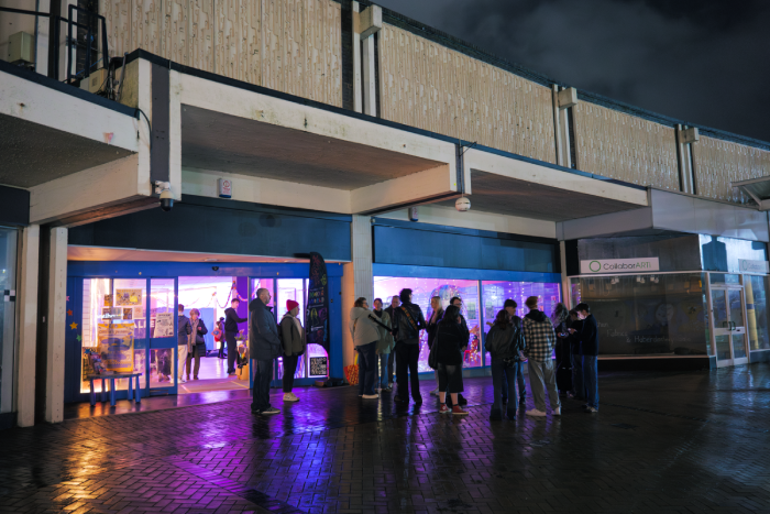 Group of people standing outside at night in front of a building with colorful neon lights inside. Event organised by Natalie Jane.