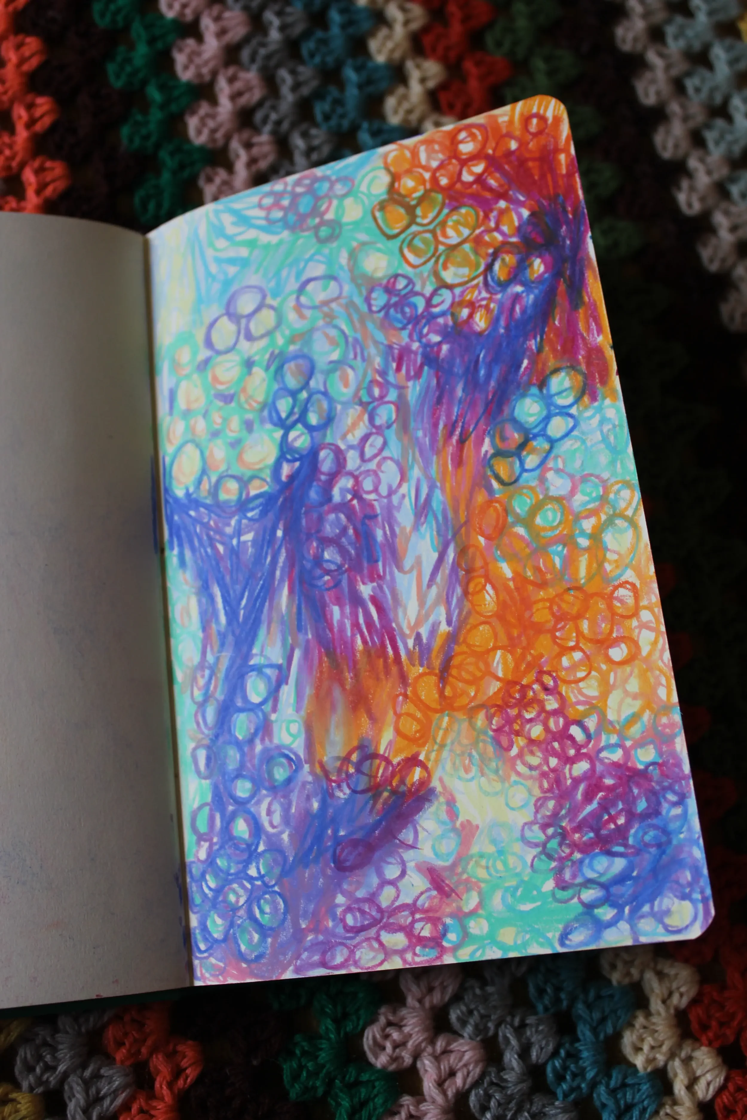 A colorful abstract drawing with swirls, circles, and scribbles in shades of orange, purple, blue, green, and red on a large page of a notebook.