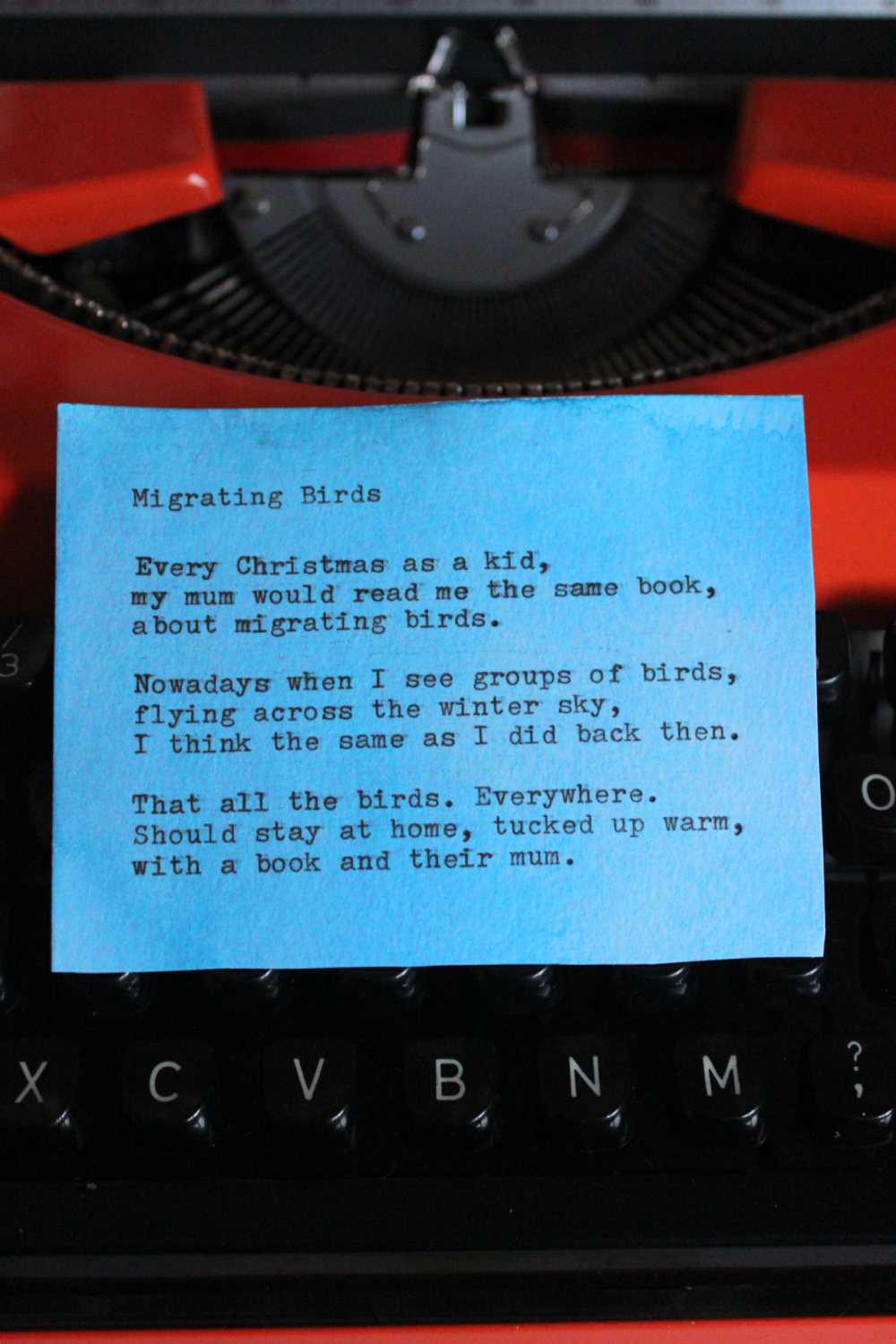 A blue note with a poem titled "Migrating Birds" placed on a black typewriter with orange accents.