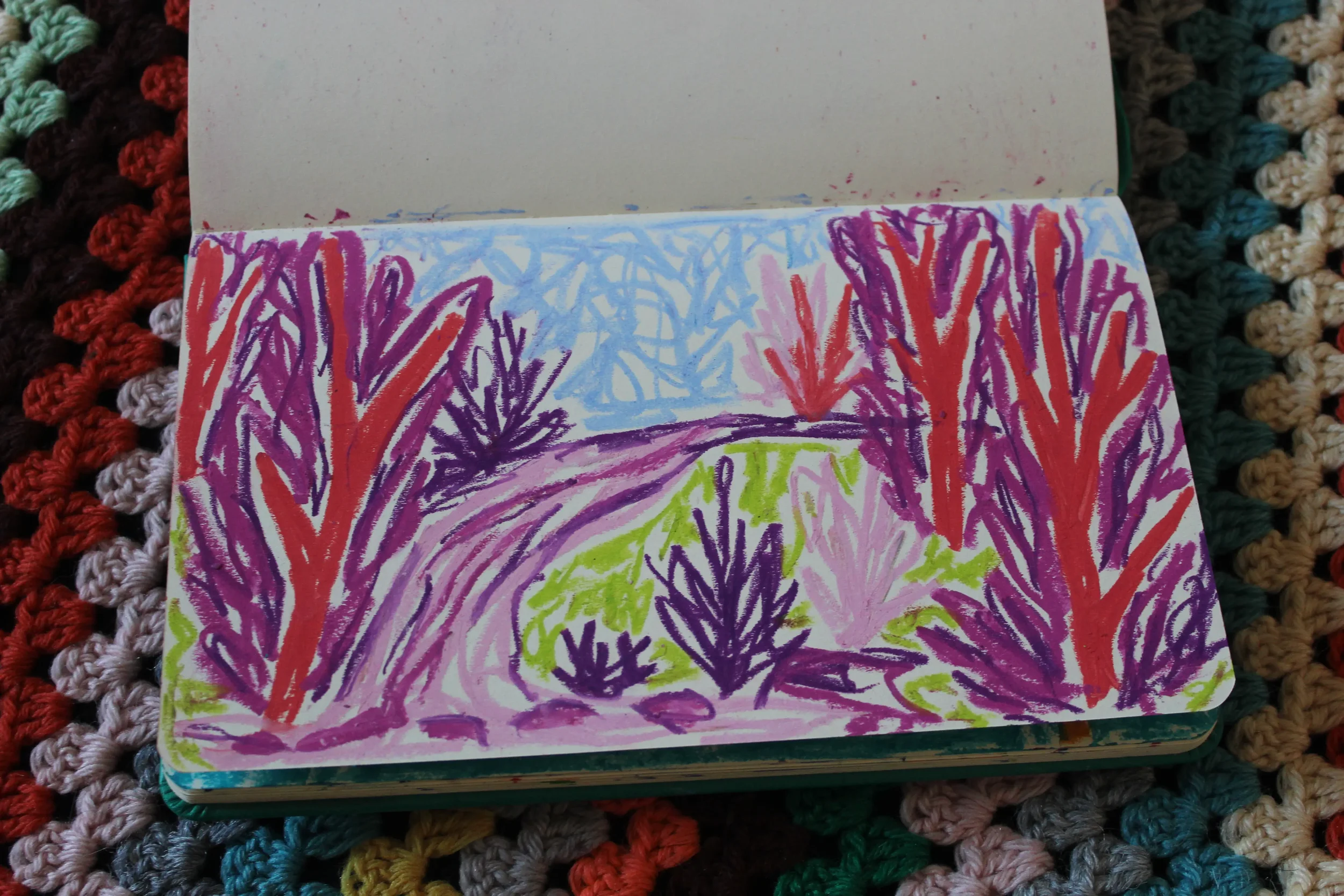 A colorful drawing on a page depicts a nature scene with trees in shades of purple, orange, and pink, and green vegetation, with a blue sky in the background.