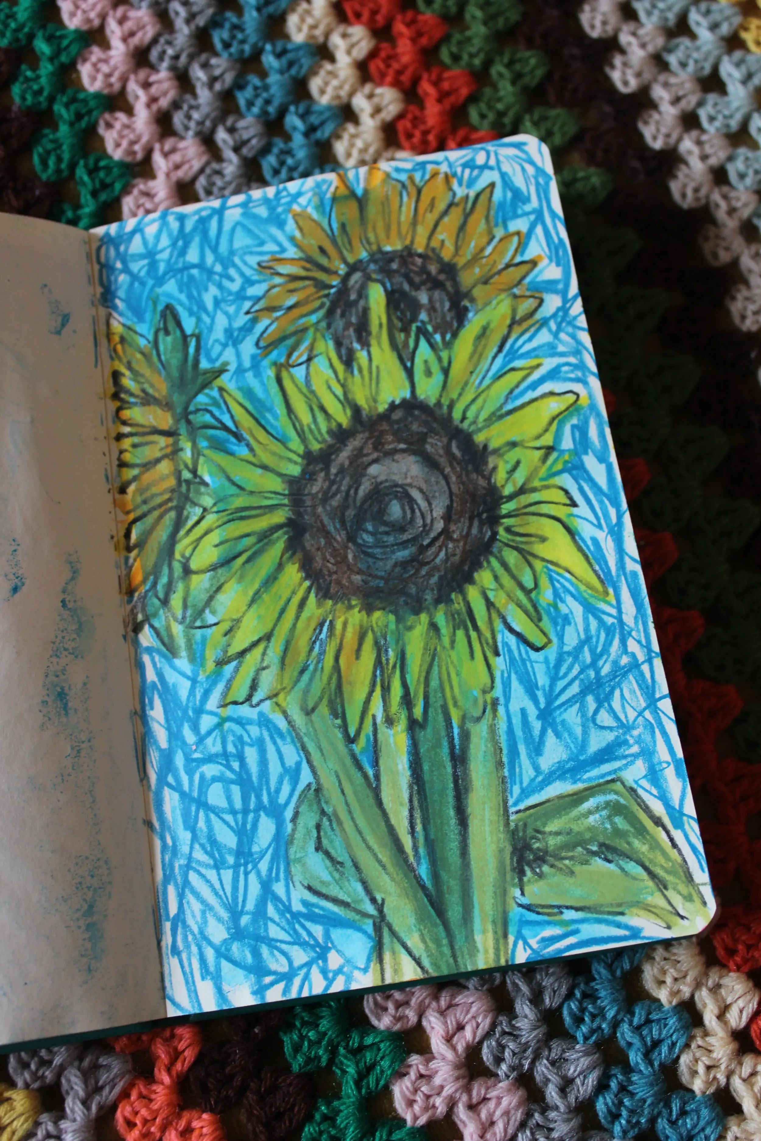 Hand-drawn illustration of a sunflower with bright yellow petals and a dark center, set against a blue background with scribbled blue lines.