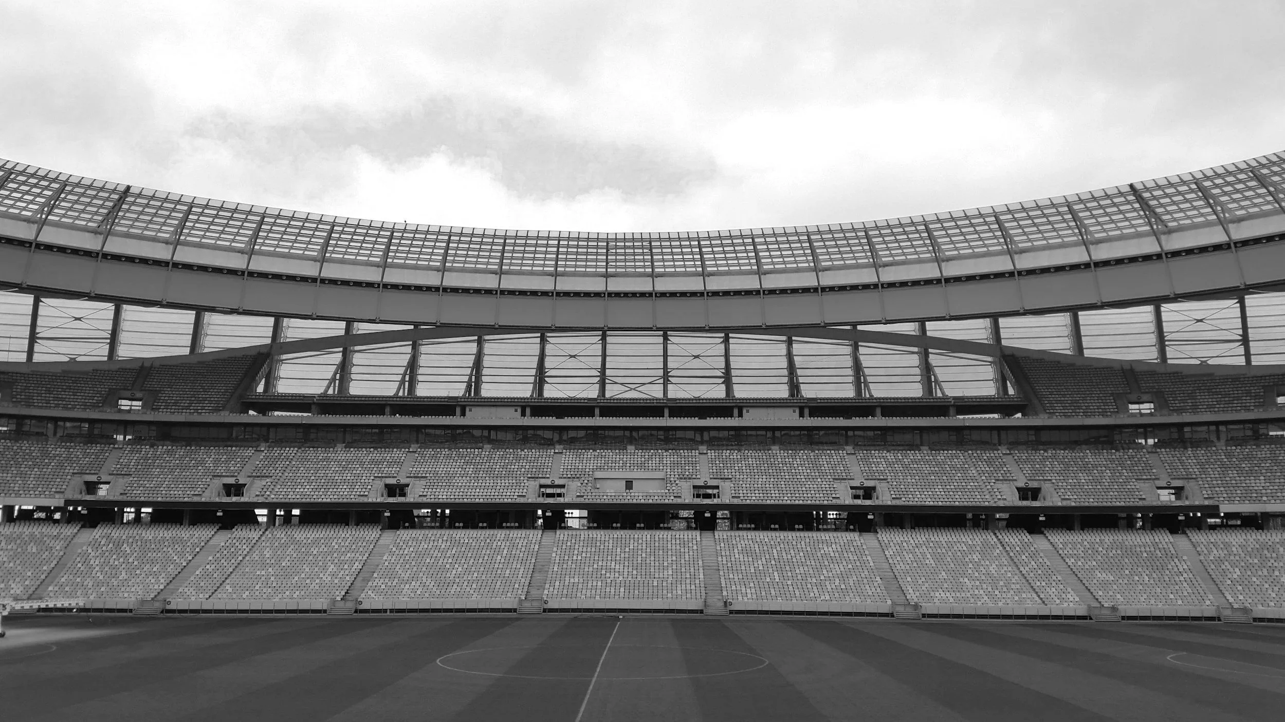 Empty stadium with empty seats, field, and overcast sky.