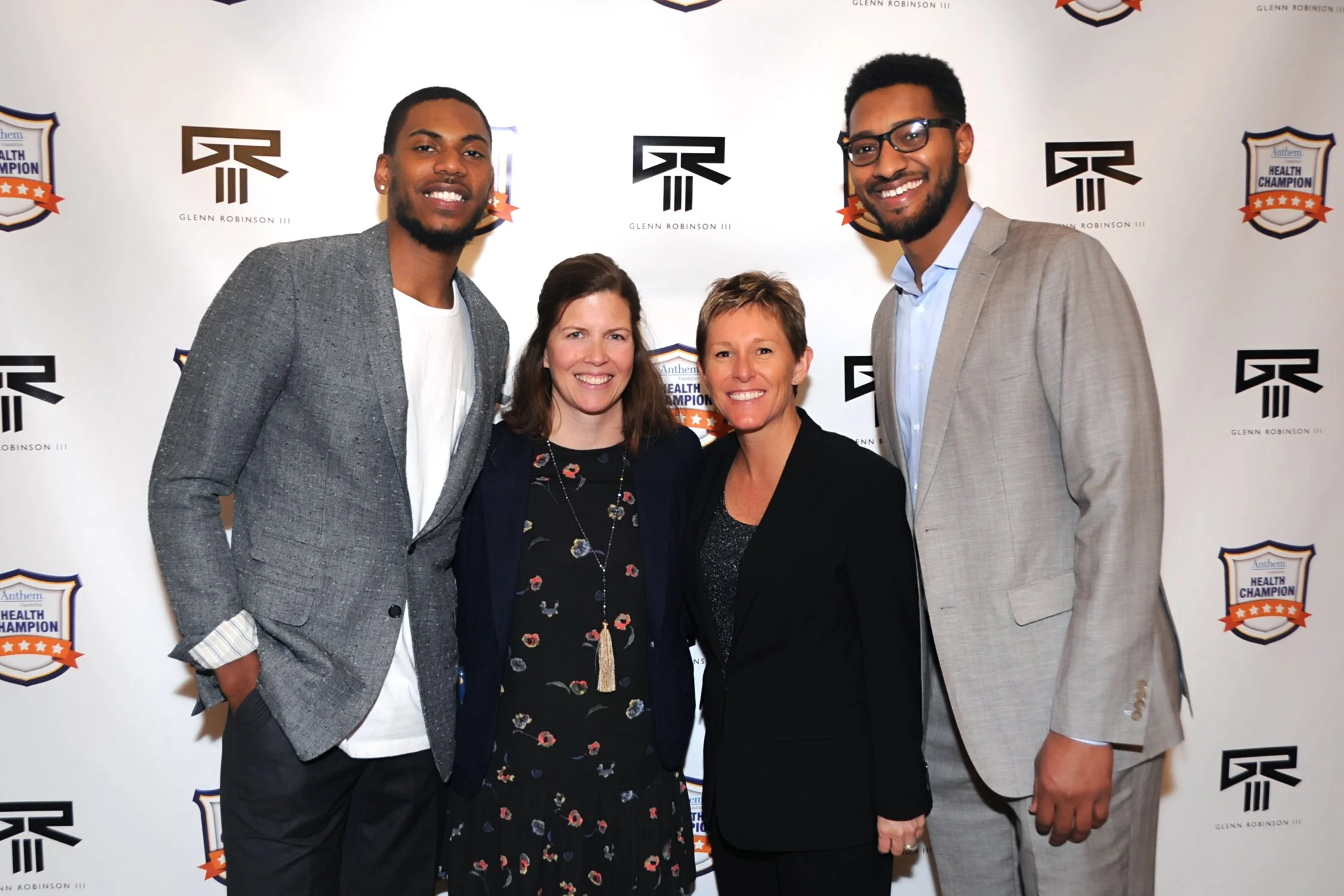 Four people, two men and two women, smiling and posing together at an event with a branded backdrop.