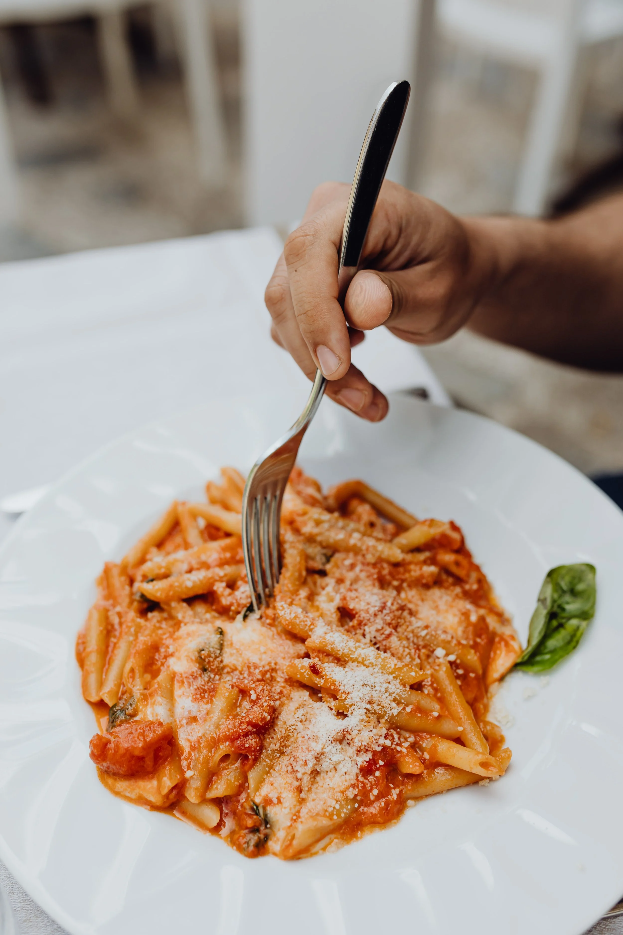 A person eating a plate of spaghetti with tomato sauce and grated cheese.