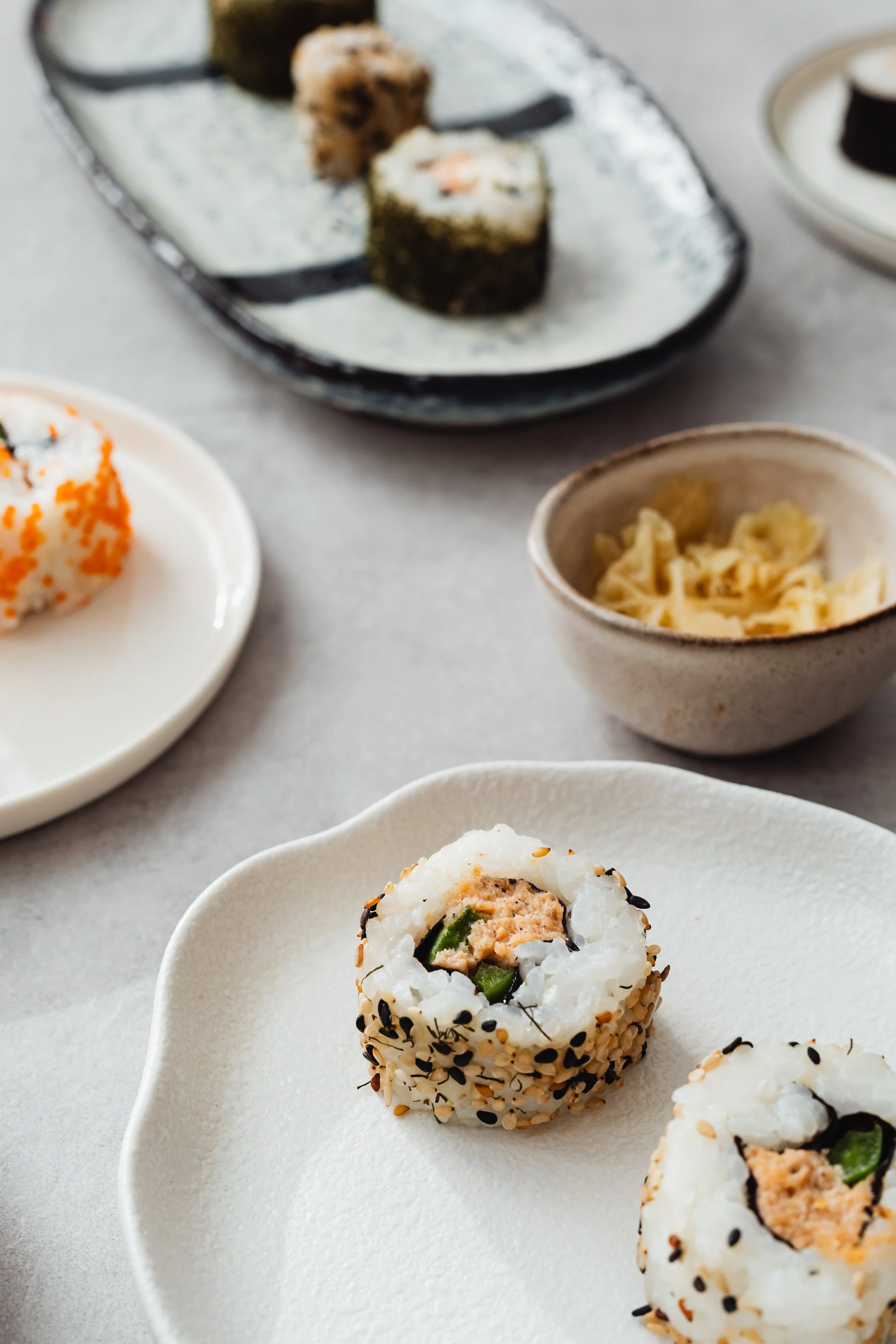 Close-up of sushi rolls on a white plate, with other sushi dishes in the background.