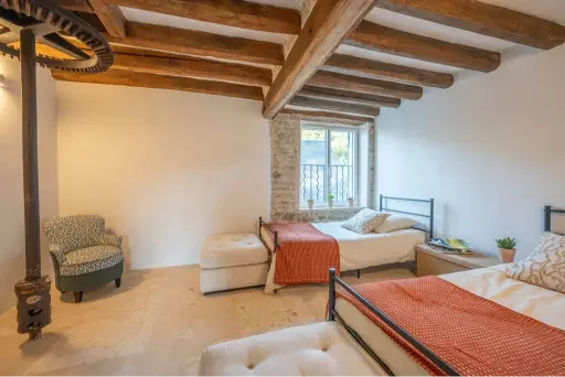 Bedroom with two single beds, a vintage armchair, a small potted plant, and exposed wooden ceiling beams.