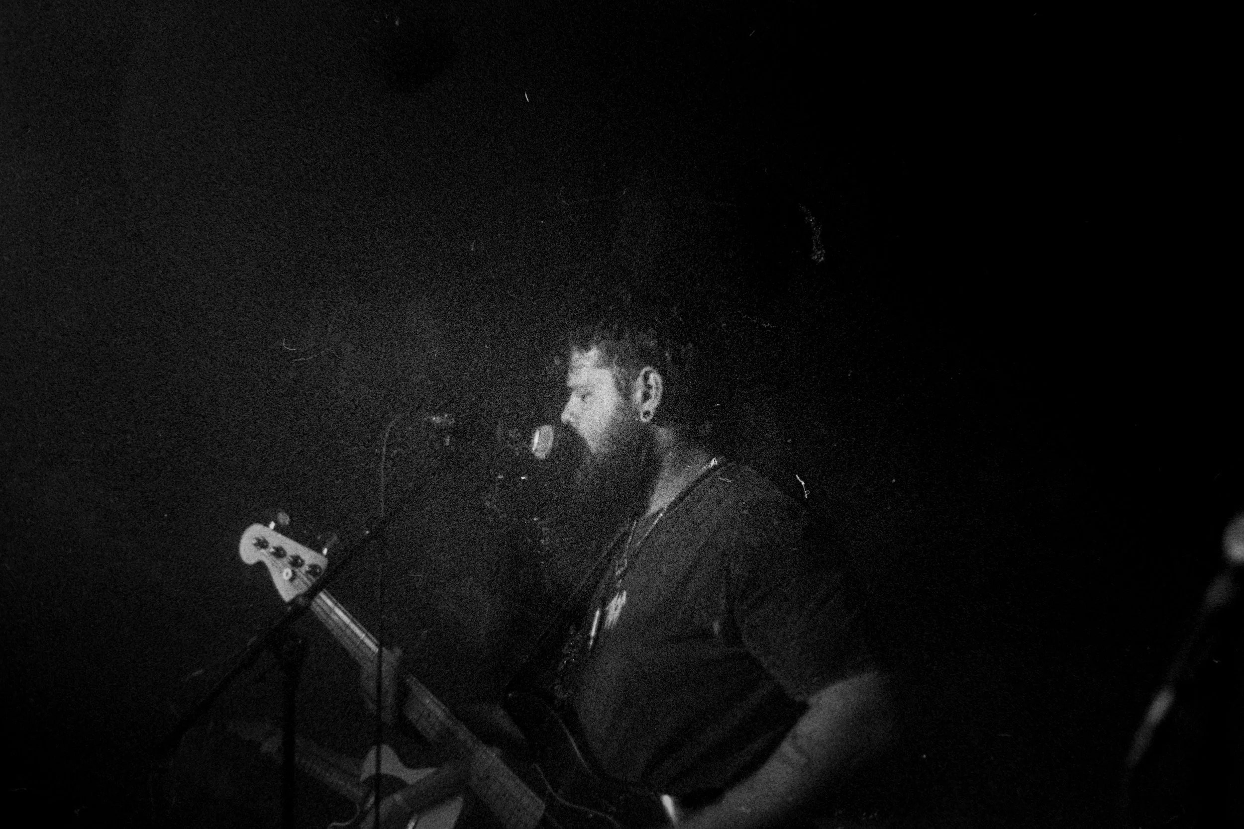 A man singing into a microphone on a dark stage, playing an electric guitar.