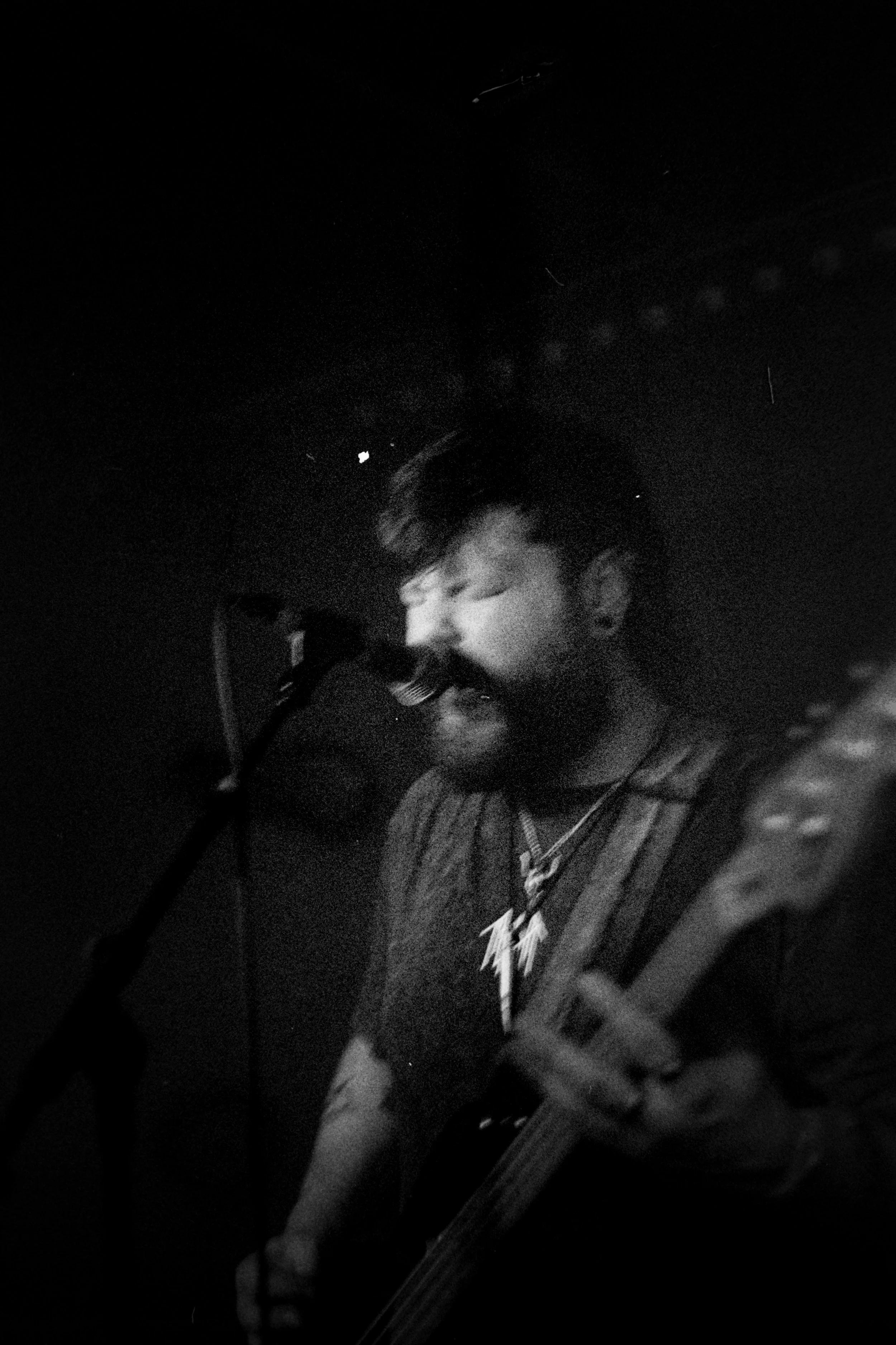 A black and white photo of a musician singing into a microphone while playing a guitar.