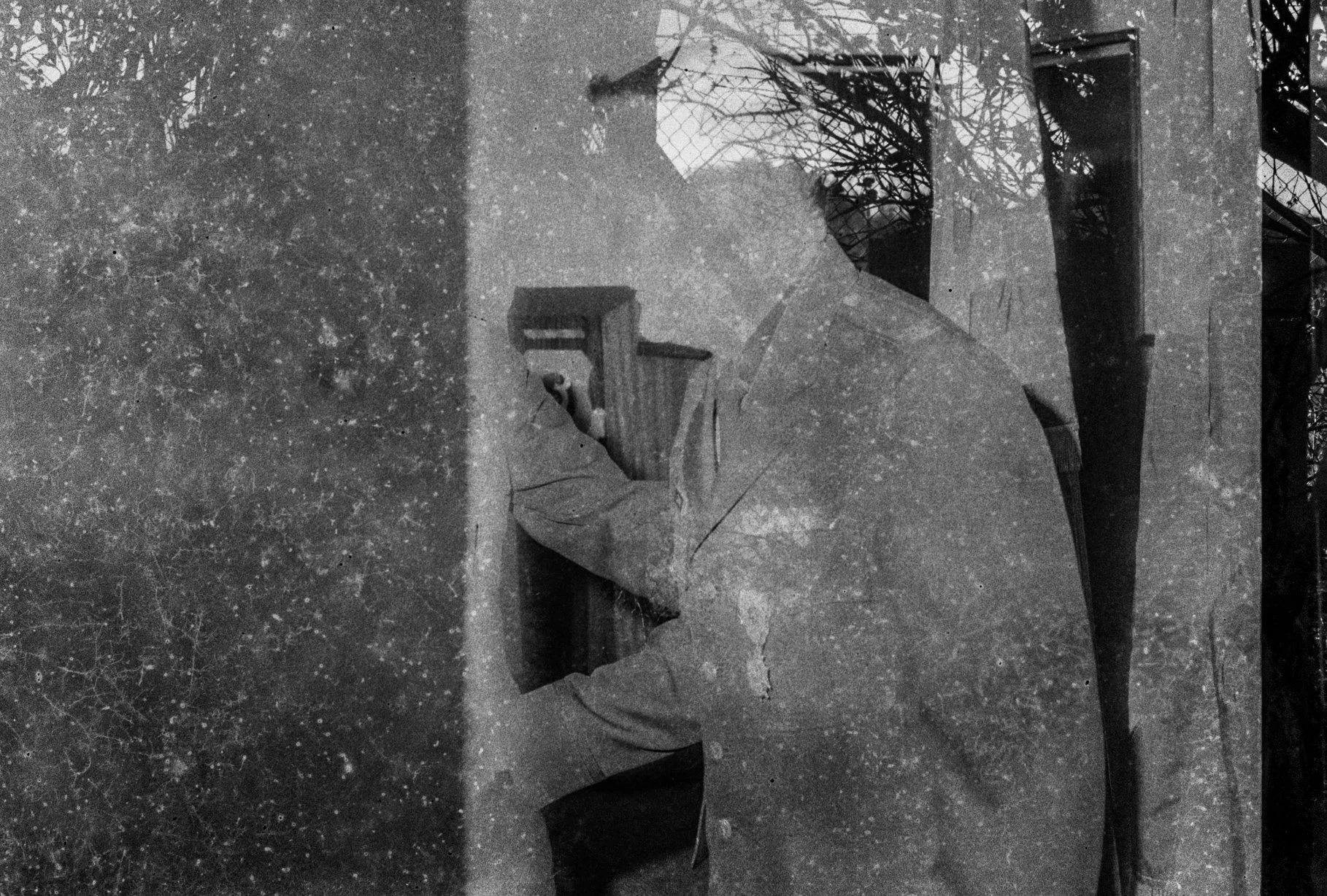A black and white photo of an old, broken statue of a seated man with a beard, wearing a hat, and resting his chin on his hand. The statue appears worn and weathered, with cracks and missing pieces.