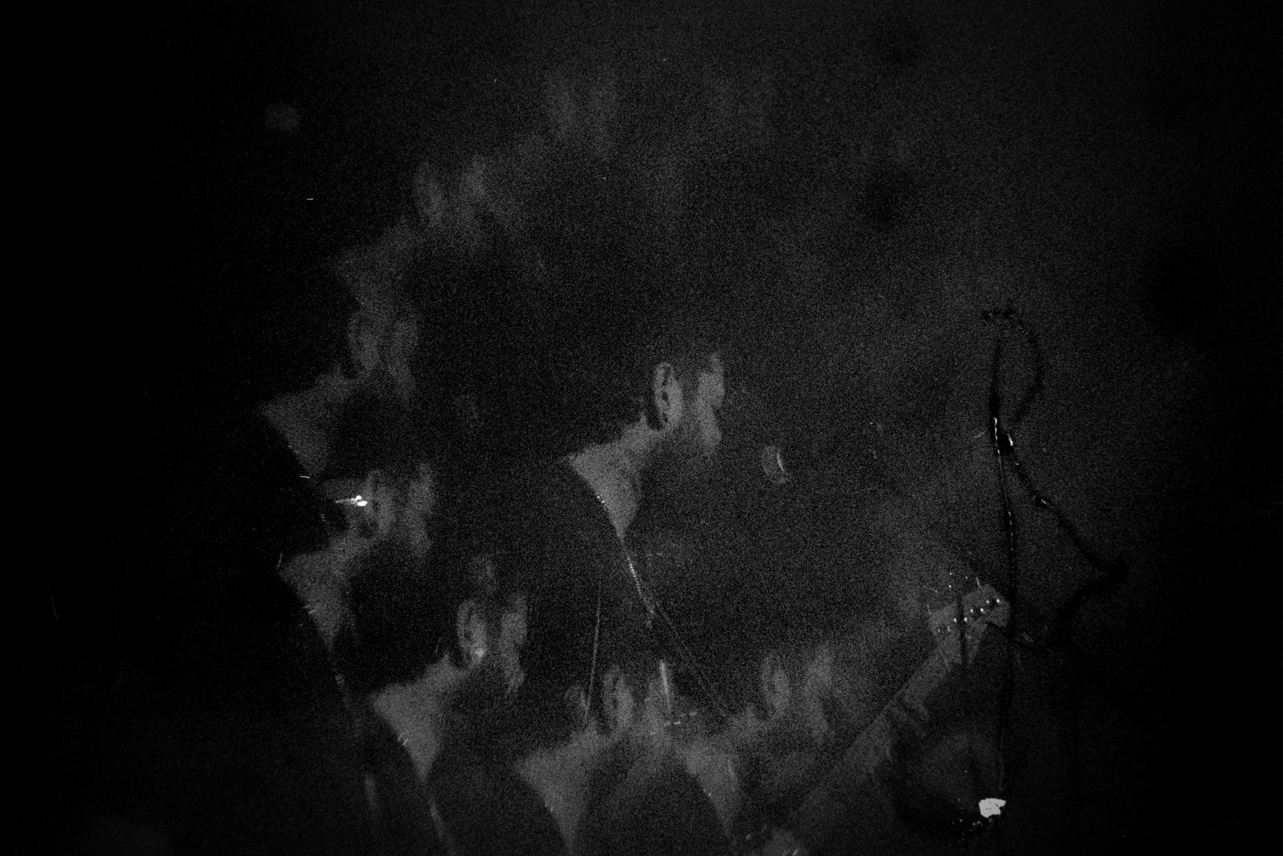 A group of people in a dark setting, possibly a concert or event, with one person standing near microphone equipment.