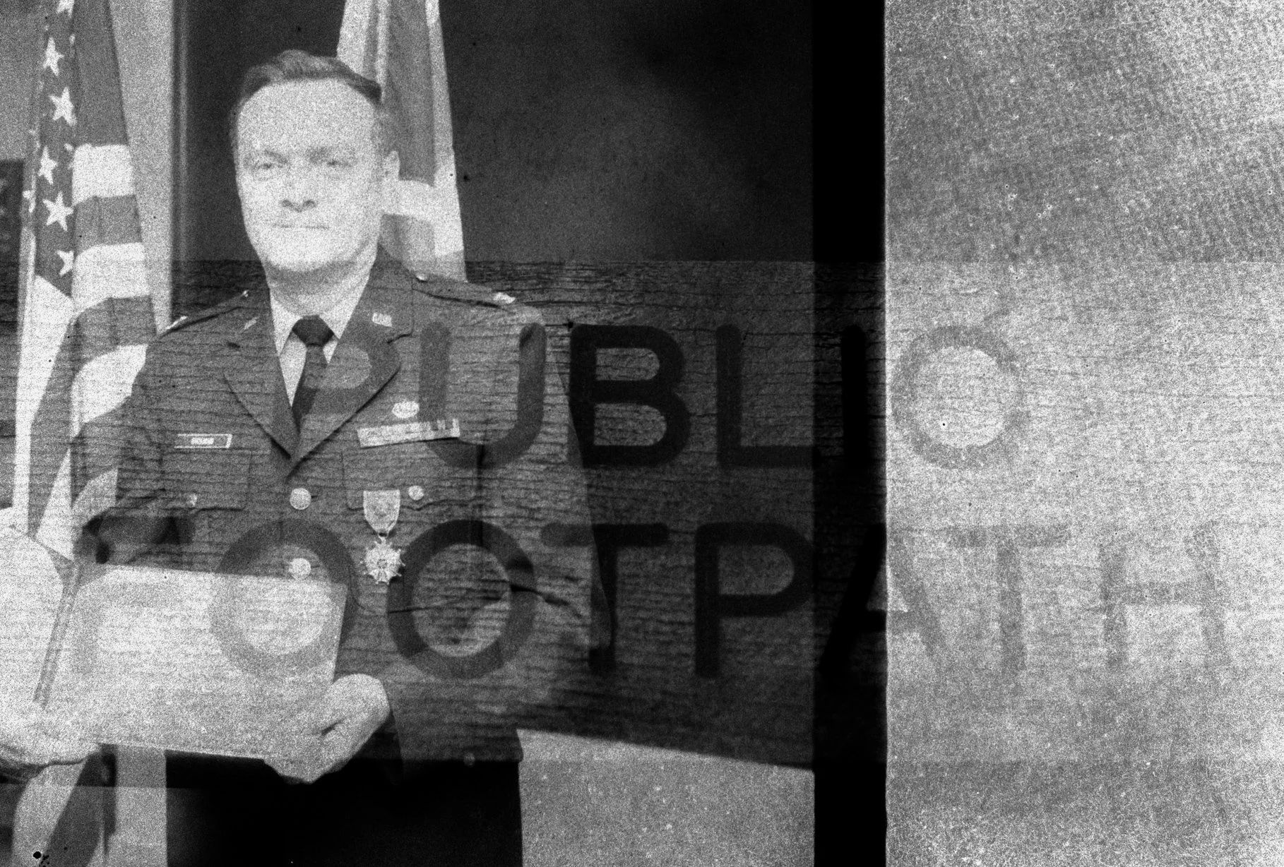 Black and white photo of a man in a military uniform holding a document, with American flags in the background, and overlapping text that reads 'PUBLIC'.