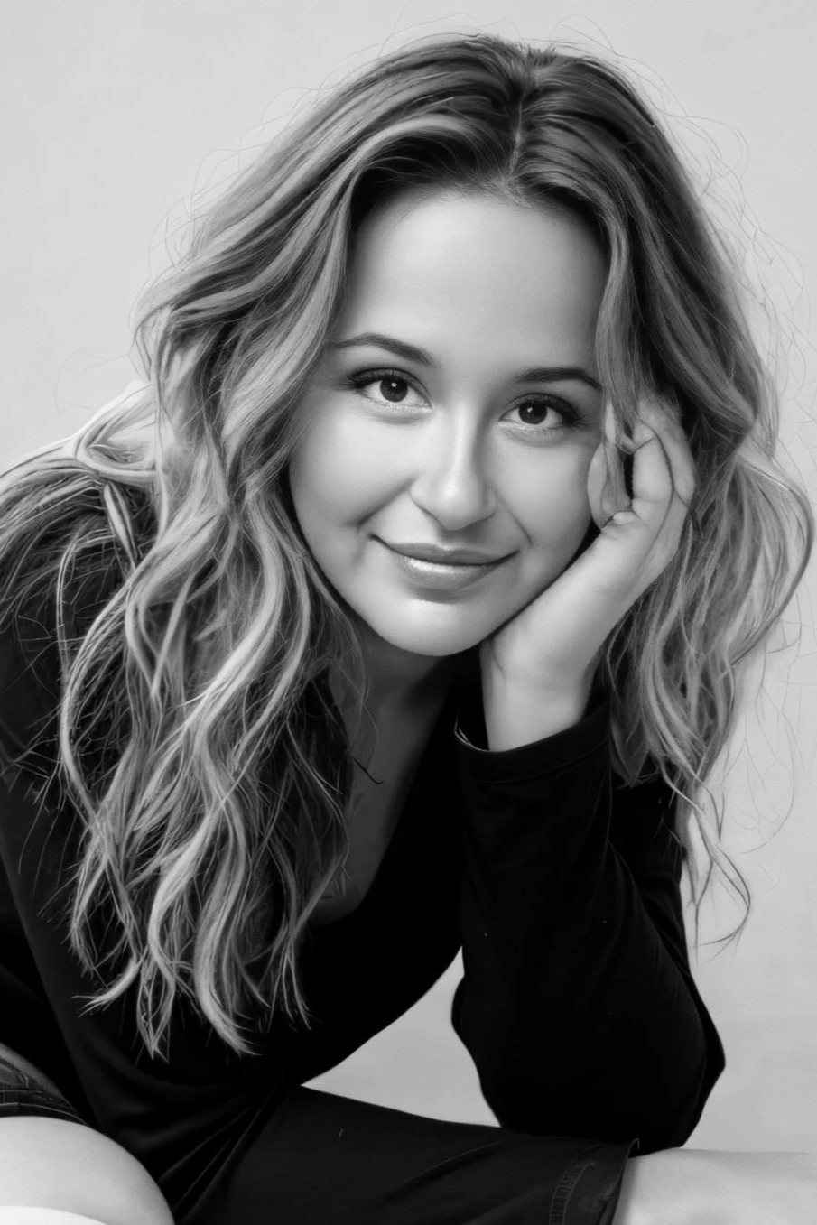 Portrait en noir et blanc d'une jeune femme avec de longs cheveux ondulés, souriante, posant avec la main sur la joue.
