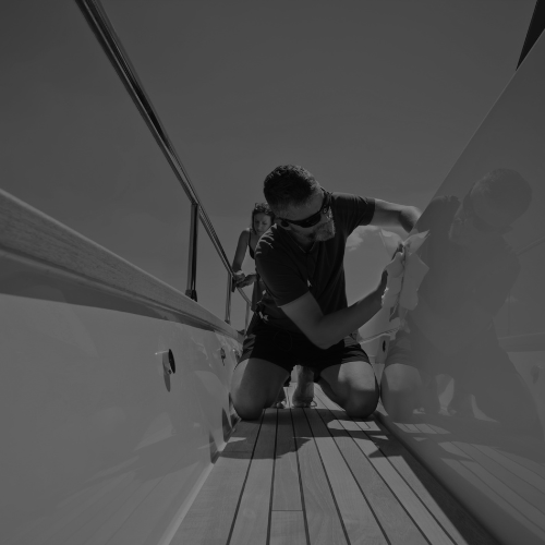Person cleaning and polishing the side of a luxury yacht on a sunny day.