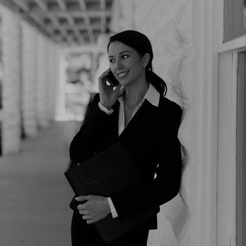 Professional businesswoman talking on a mobile phone while holding a folder in an outdoor walkway.