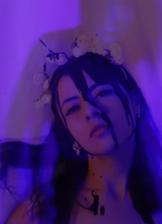 Mujer con maquillaje artístico y corona de flores con fondo morado.