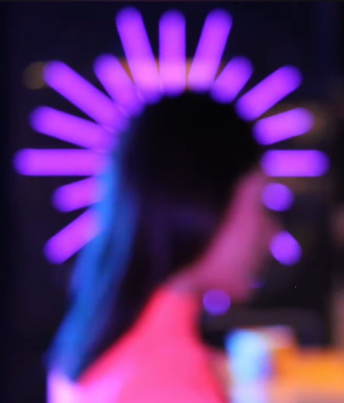 Persona con aura de luces moradas y rosadas en forma de corona, vista borrosa en un ambiente oscuro.