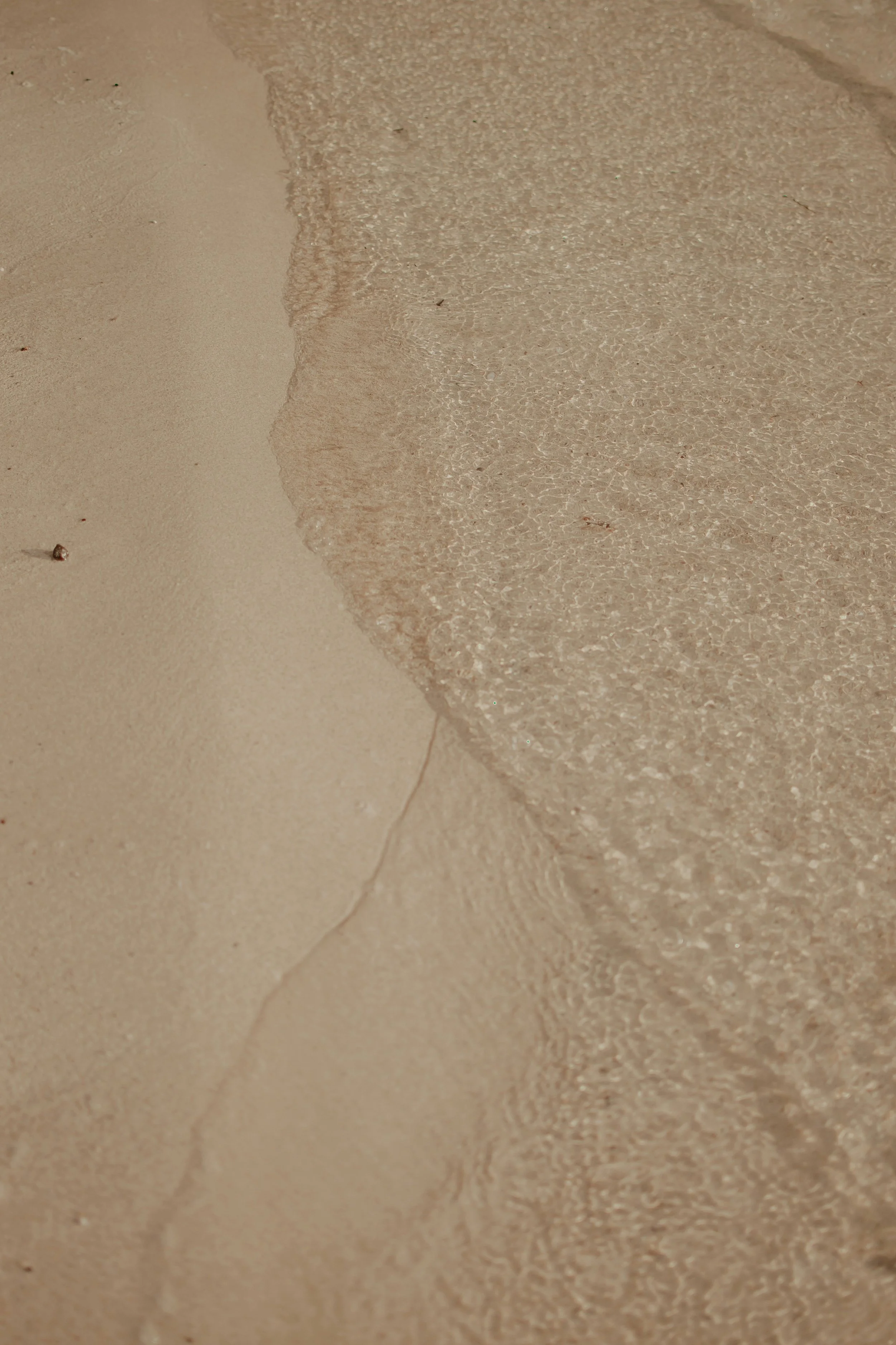 Close-up of gentle waves with white foam on a sandy beach.