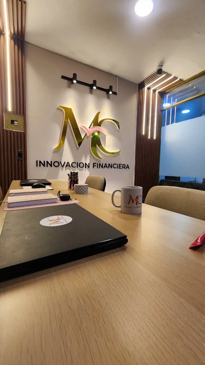 Sala de reuniones con logo de Innovación Financiera en la pared, escritorio con documentos, una taza y objetos de oficina.