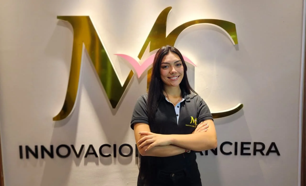 Mujer joven sonriendo con brazos cruzados frente a un logo en una pared, que dice 'Innovación Financiera'.