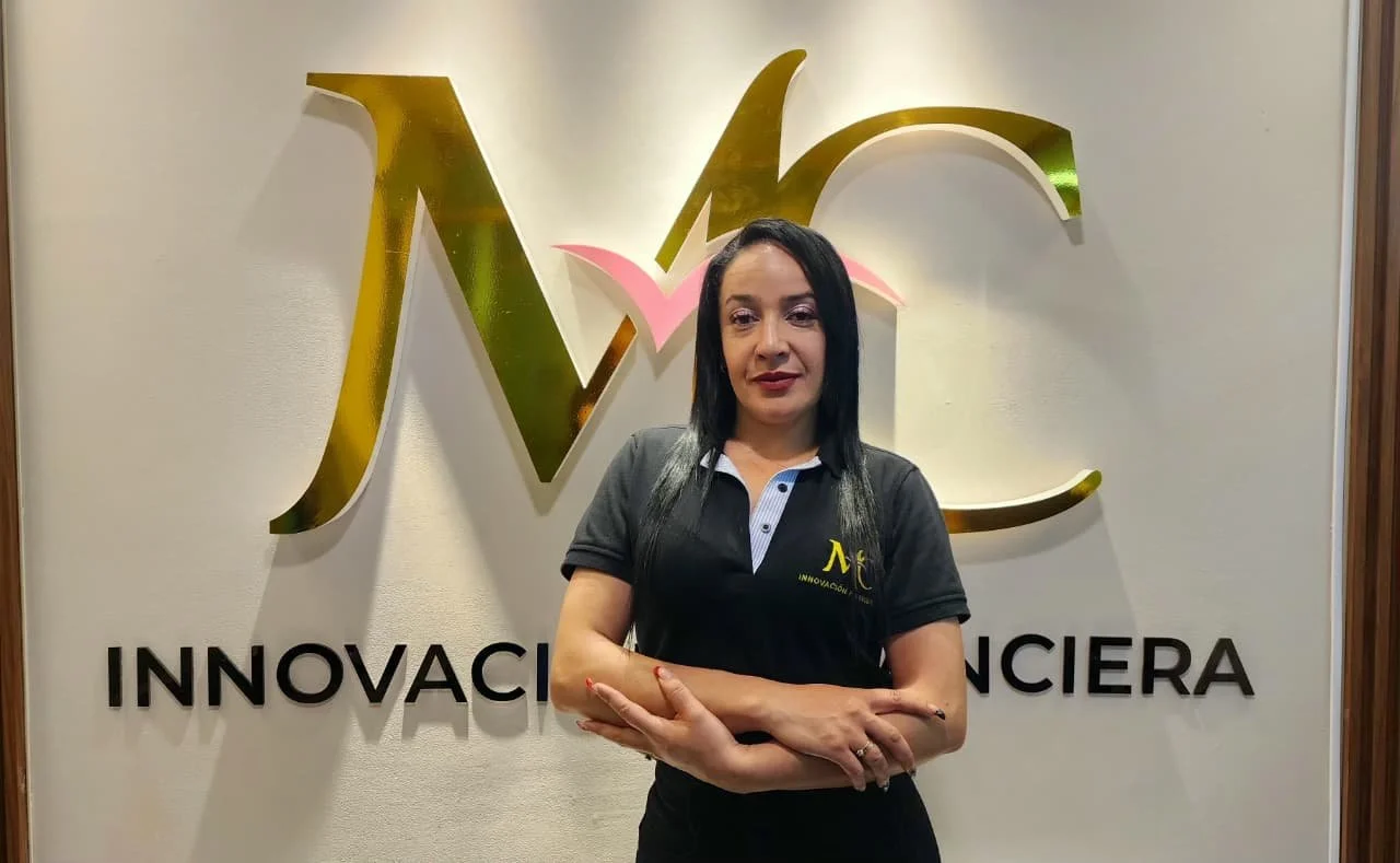 Mujer de cabello oscuro con uniforme negro en frente de un logo dorado y rosa que dice 'Innovación Financiera' en un muro blanco.