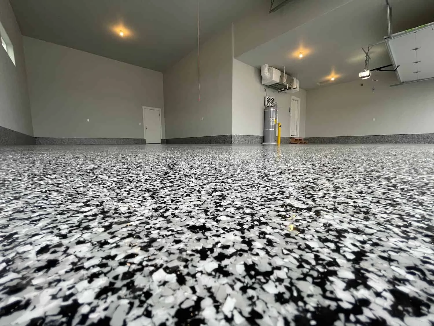 Empty garage with a speckled black and white epoxy floor, plain gray walls, and ceiling with recessed lighting.